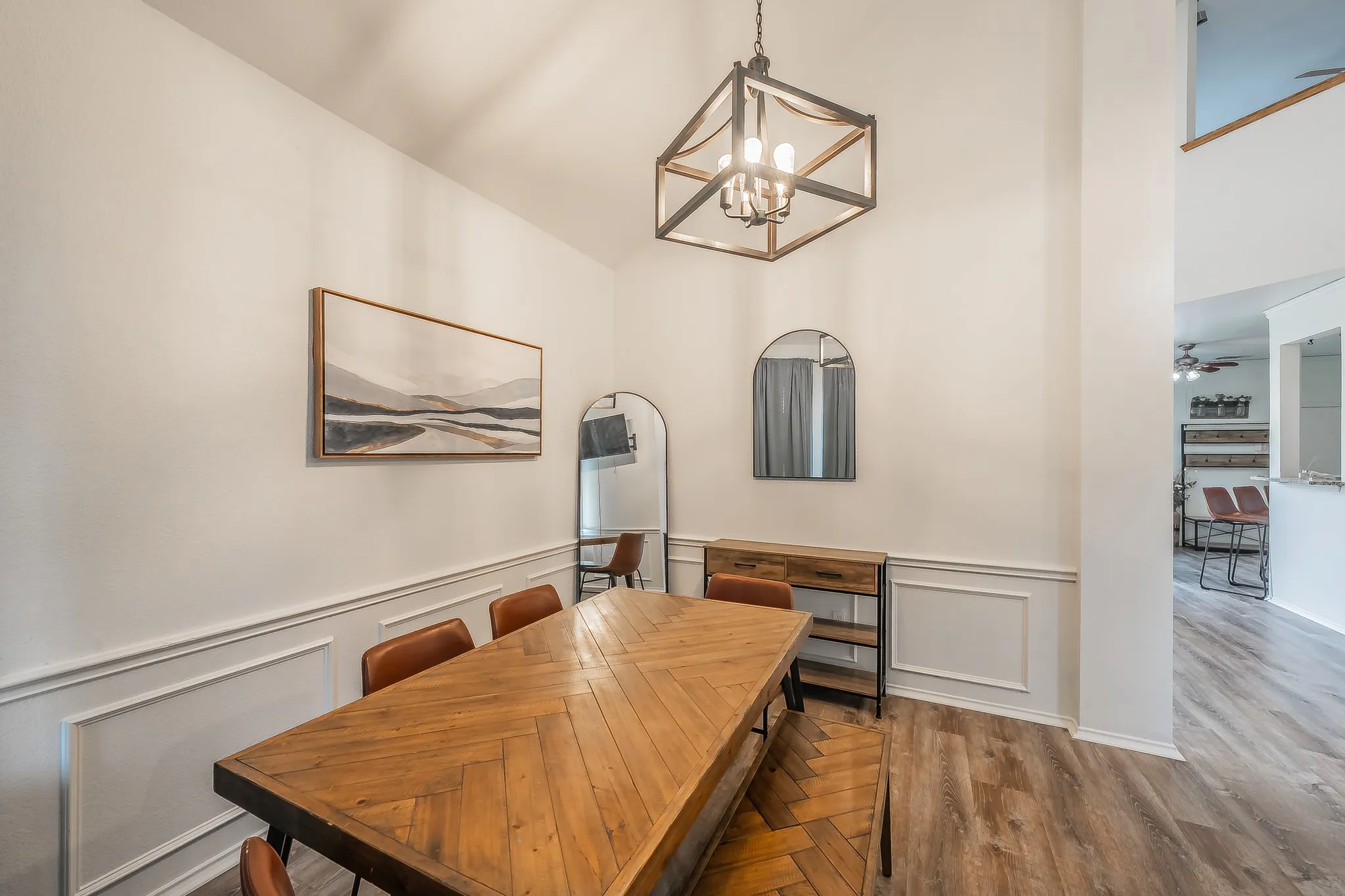 Dining area featuring vaulted ceilings, wood-finish flooring, and wainscoting with decorative trim