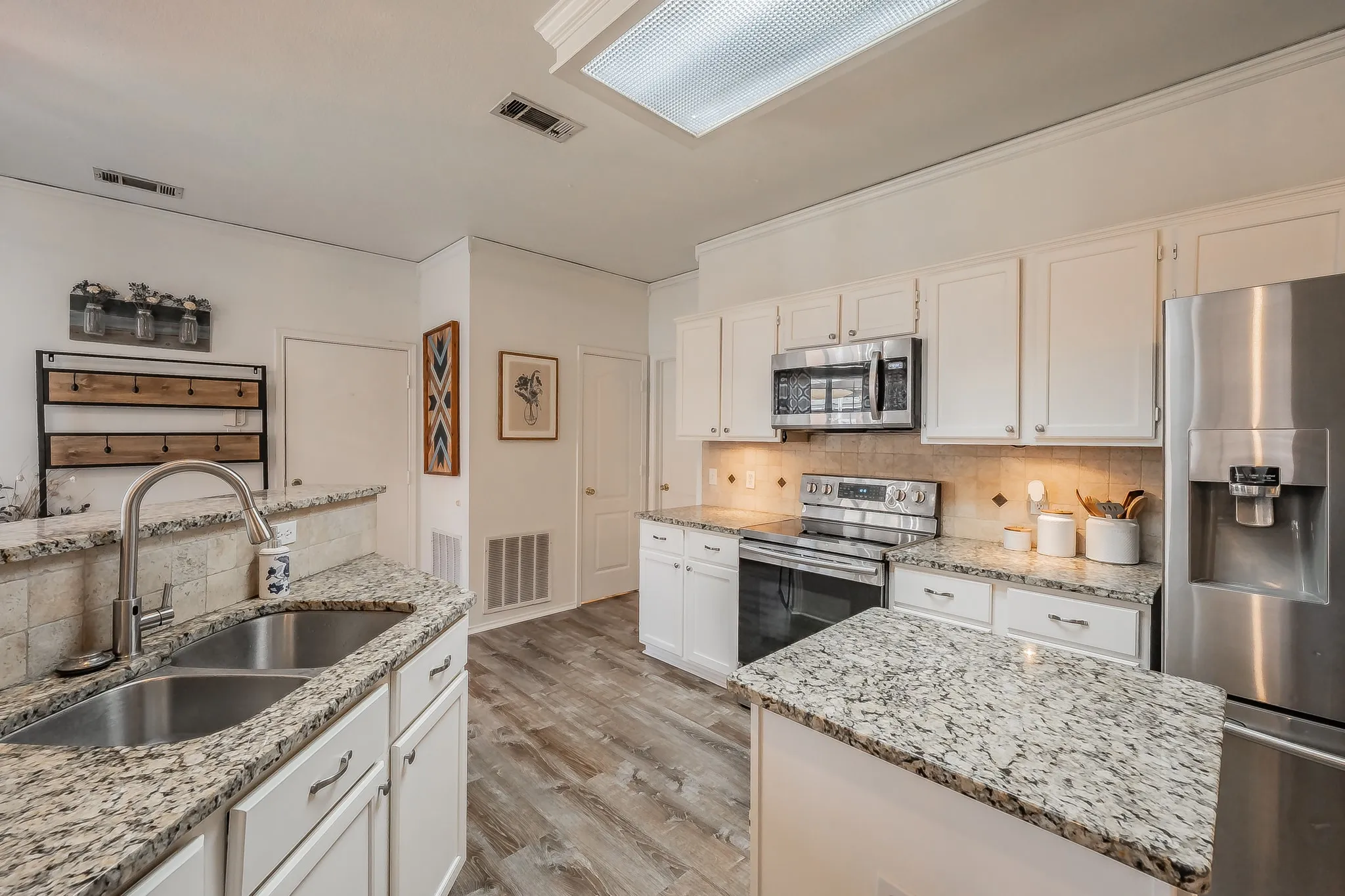 Kitchen featuring white cabinetry, wood-finish flooring, stainless steel appliances, granite countertops, and a tile backsplash