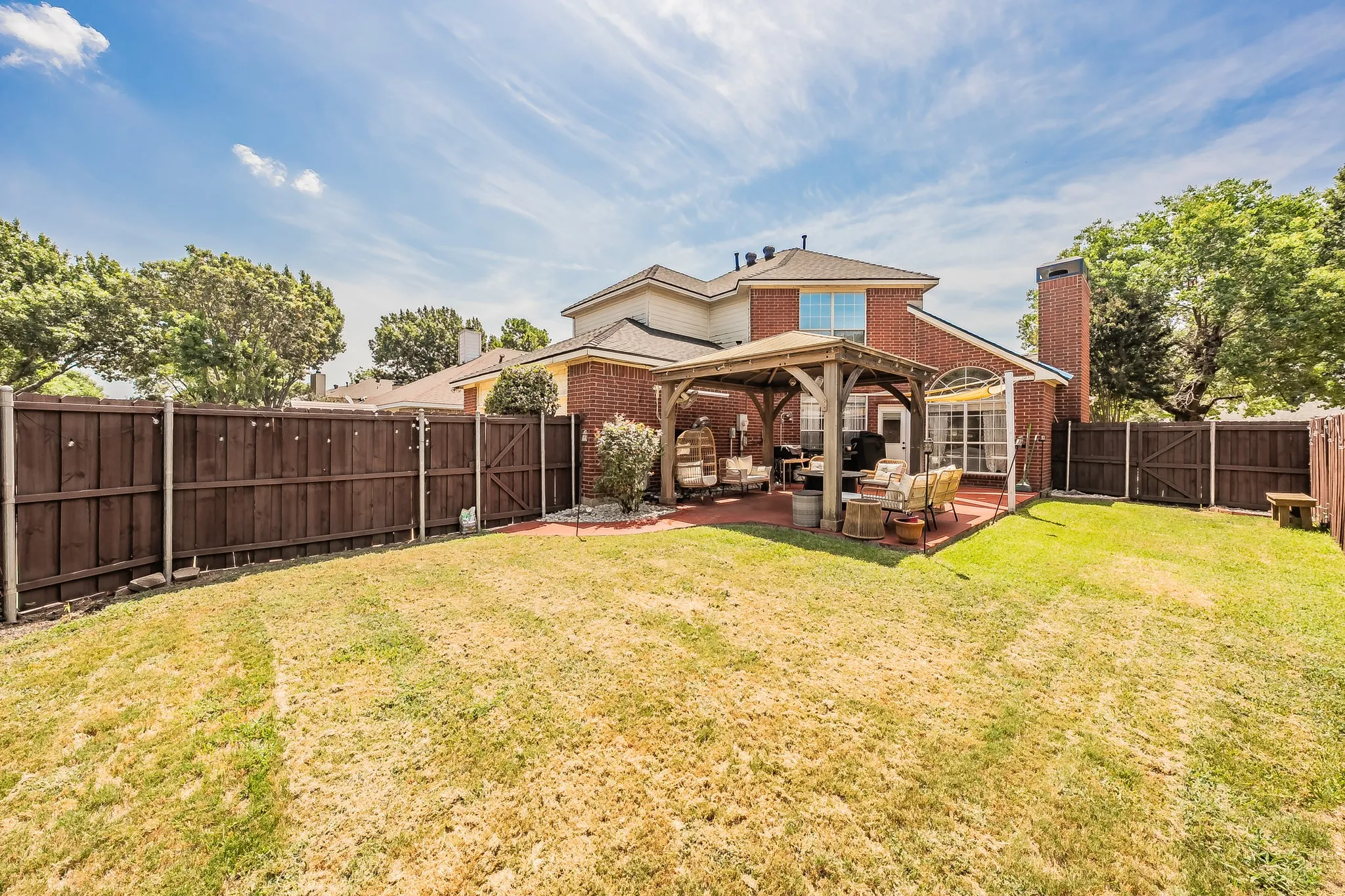 Expansive backyard featuring a large grass area, a wooden privacy fence, and a covered patio with a gazebo structure