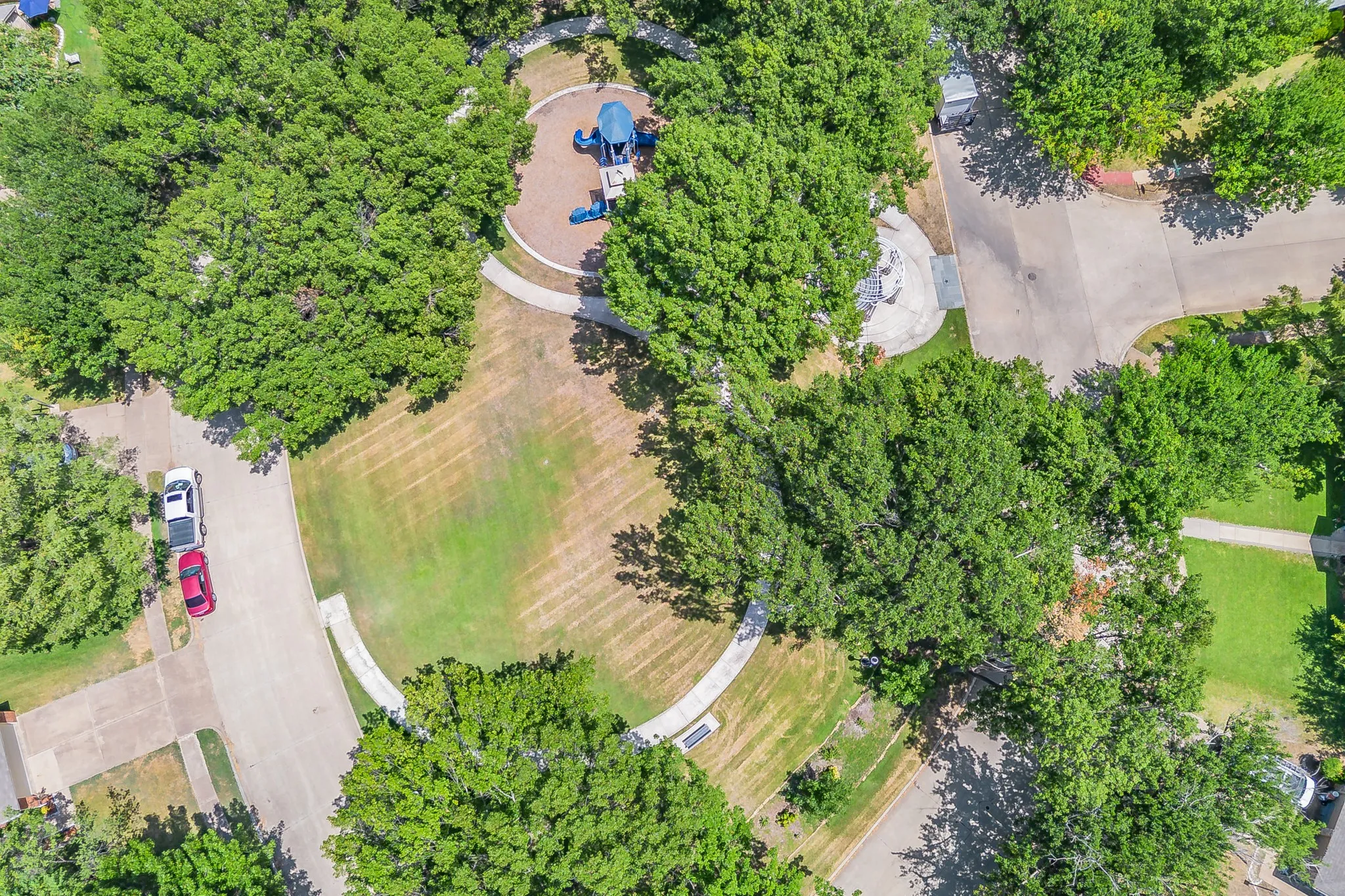 Circular green space featuring a playground with blue equipment, surrounded by mature trees