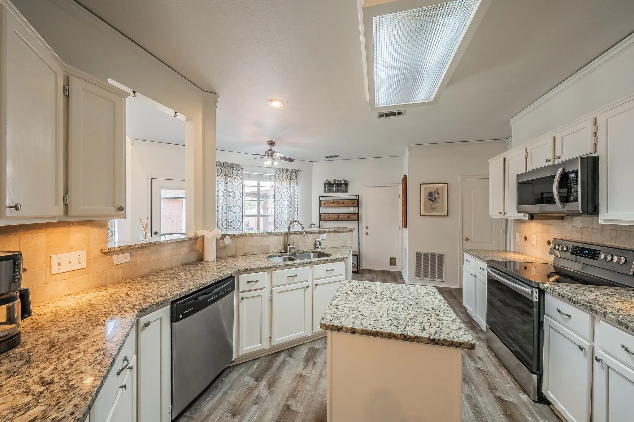 Kitchen featuring a central island, wood-finish flooring, white cabinetry, granite countertops, and stainless steel appliances
