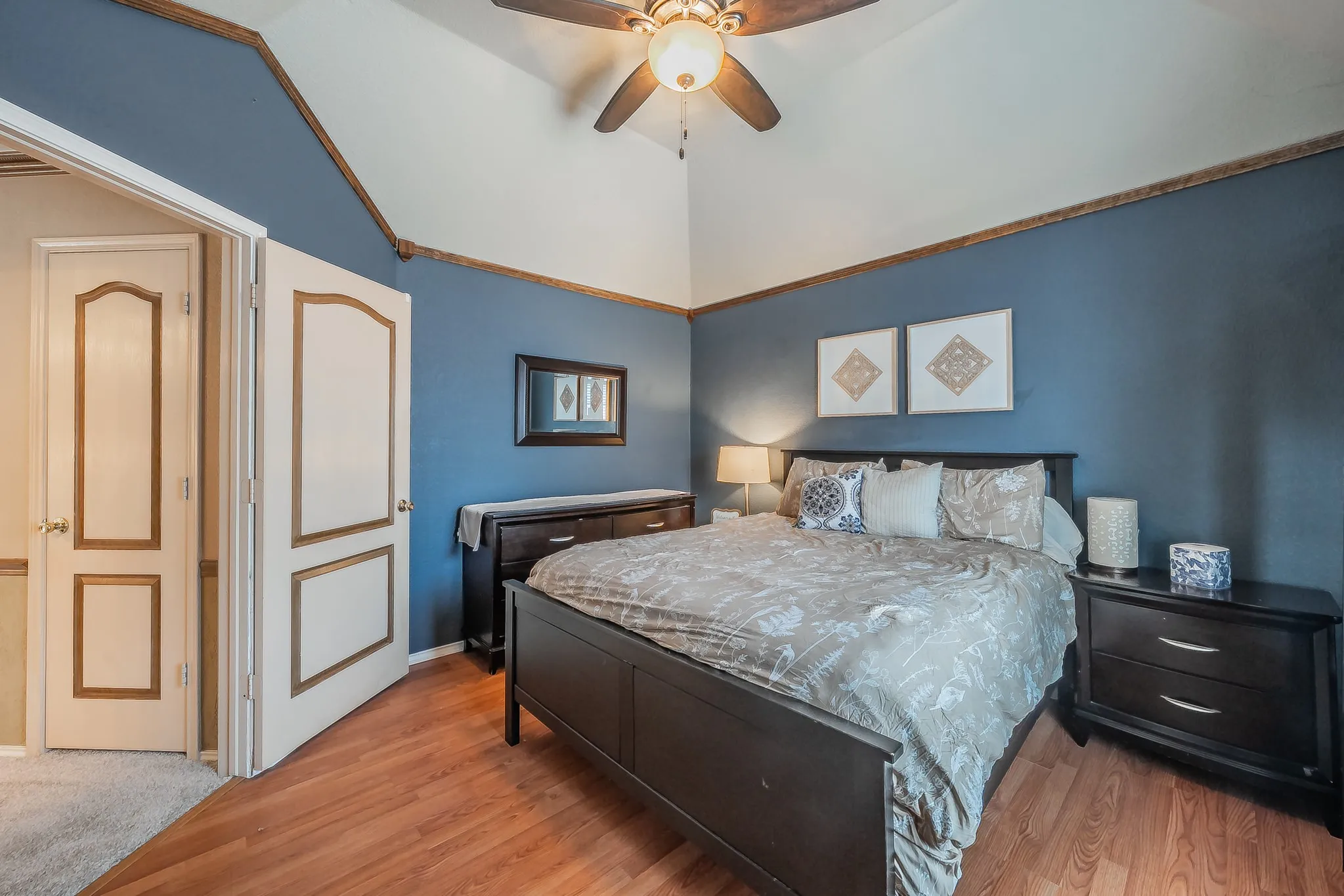 Spacious room featuring vaulted ceilings, a ceiling fan with integrated lighting, wood-finish flooring, and a paneled door with decorative trim