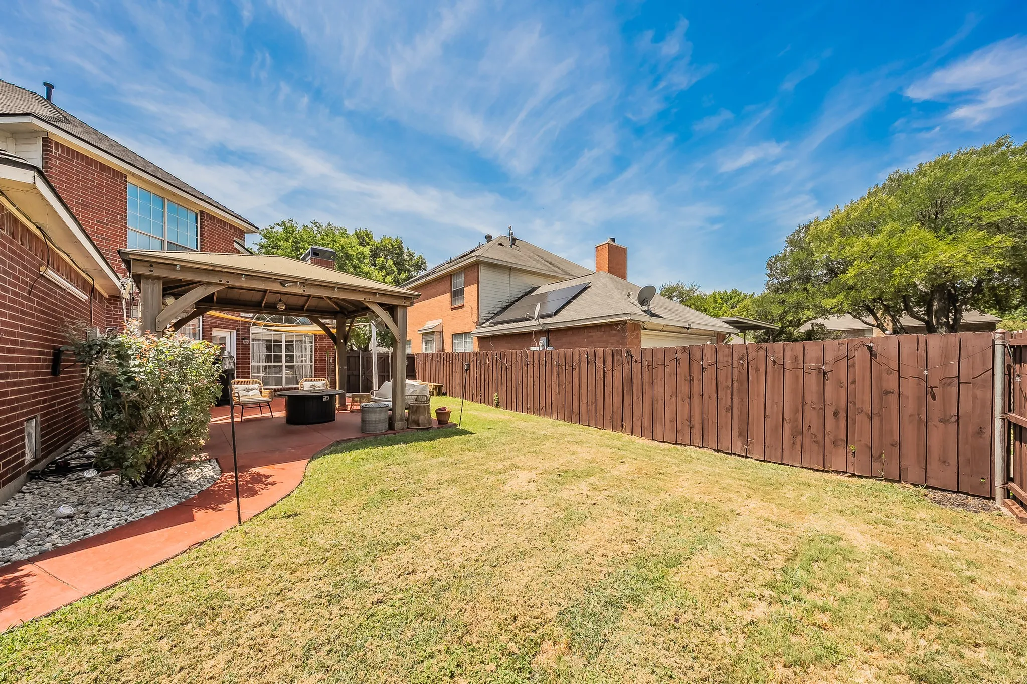 Expansive backyard featuring a large green space, a red concrete patio, a wooden gazebo, and a tall privacy fence
