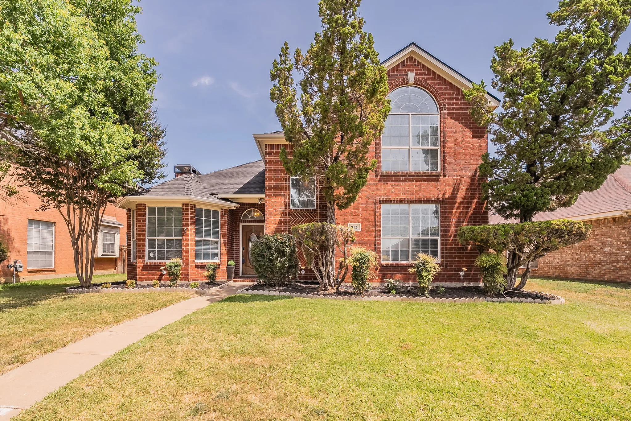 Two-story brick exterior featuring a prominent arched window, bay window, and gabled roofline