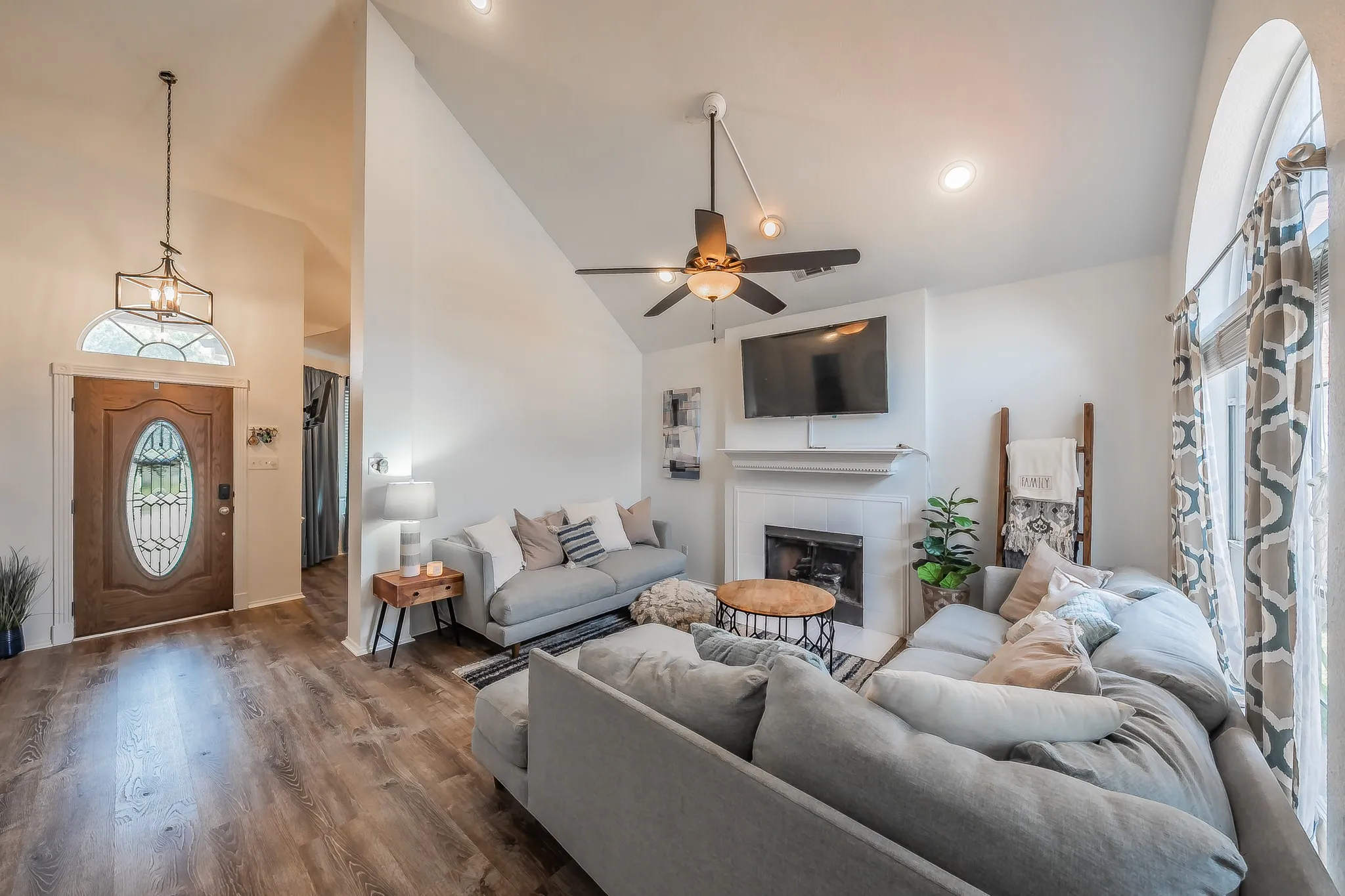 Vaulted ceilings accent this living area featuring a fireplace with a white mantel, ceiling fan, recessed lighting, and wood-finish flooring