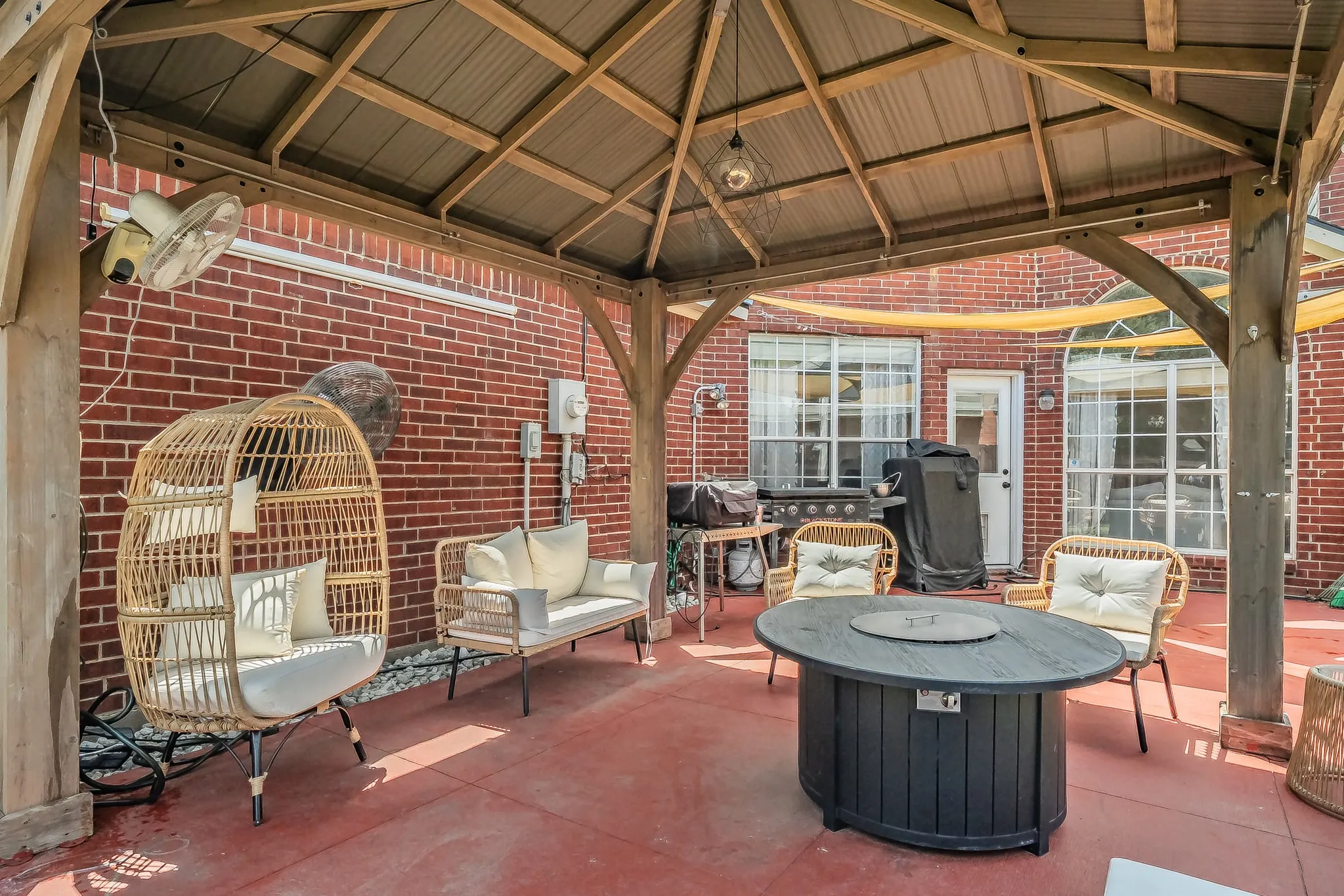 Covered patio featuring a wood-frame gazebo with a corrugated metal roof, red brick exterior walls, and a red-toned concrete slab