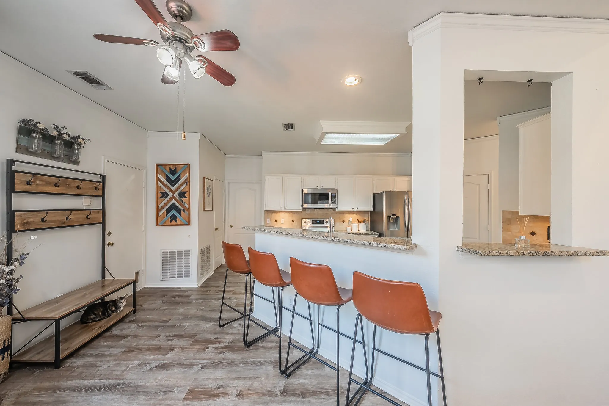 Open-concept living area featuring wood-finish flooring, a ceiling fan with integrated lighting, and a breakfast bar with a granite countertop