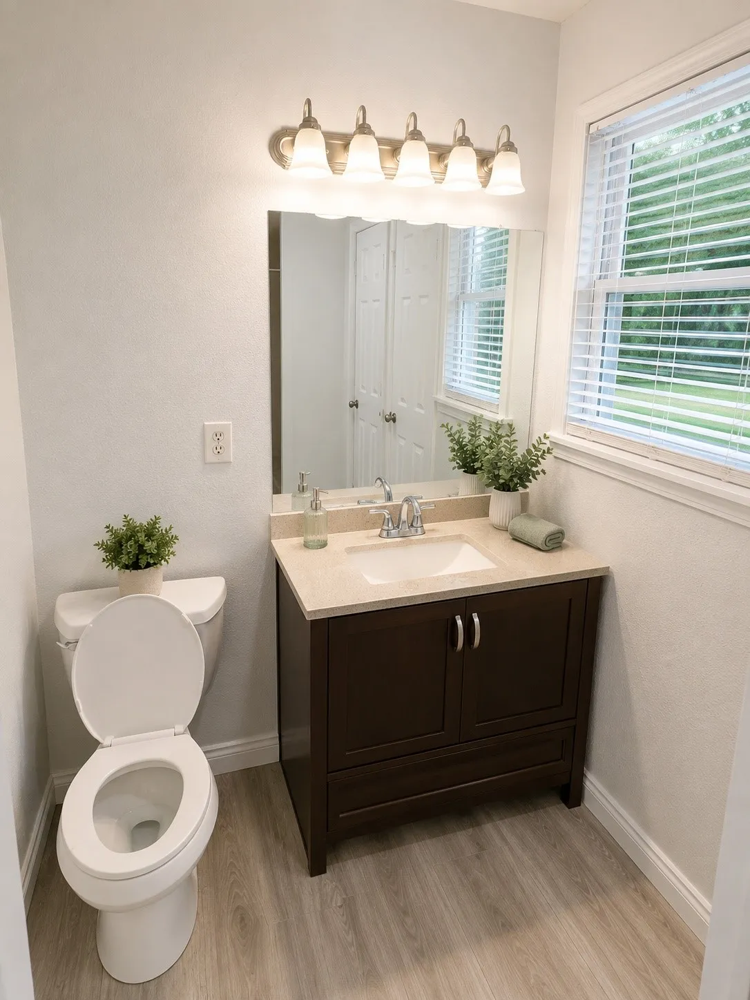 Bathroom featuring a vanity with a light-toned countertop and dark wood cabinetry, a rectangular sink with chrome fixtures, a large mirror with a decorative edge, and light wood-finish flooring