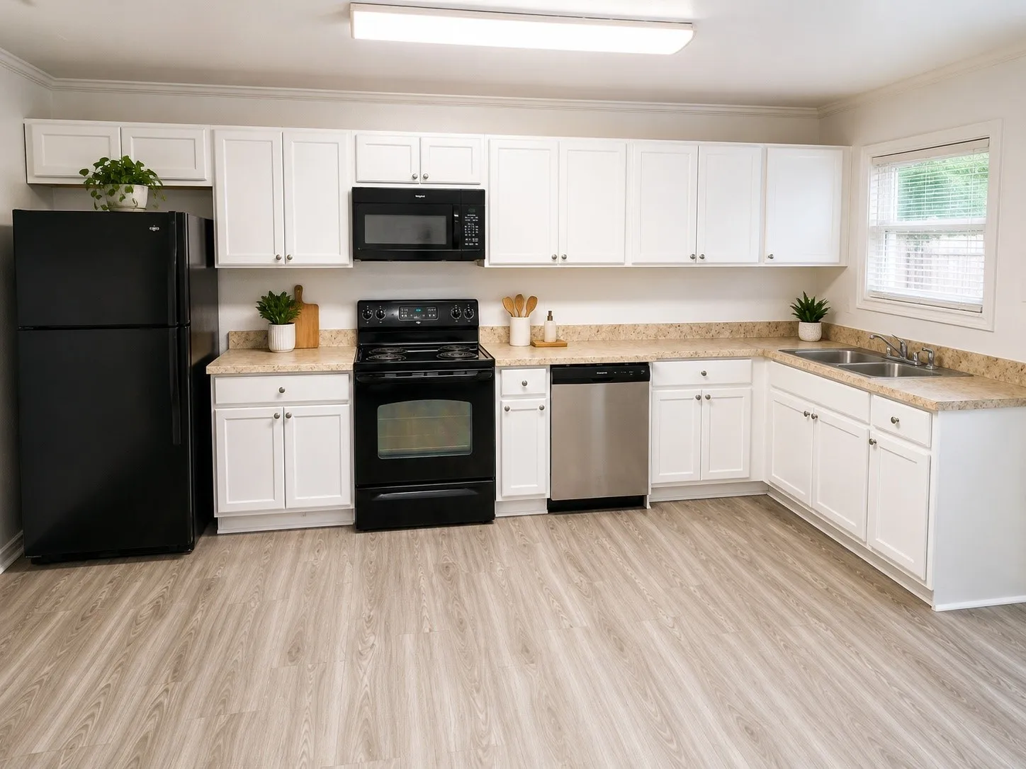 Kitchen featuring white cabinetry, wood-finish flooring, light-toned countertops, a black refrigerator, and a stainless steel dishwasher
