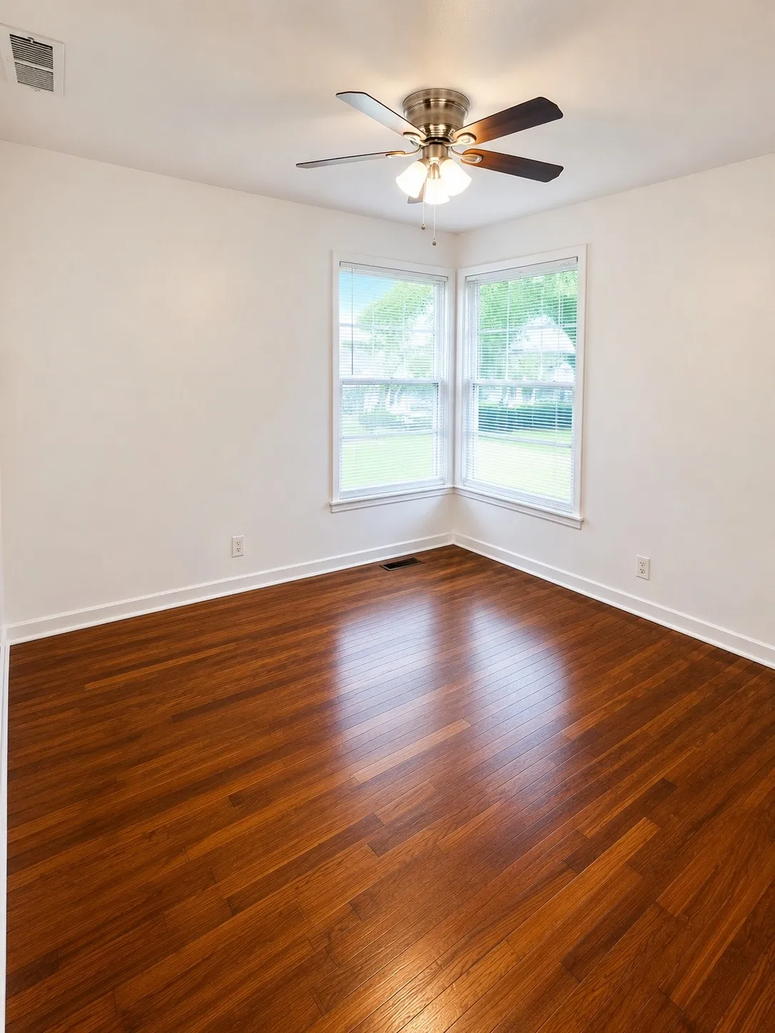 Interior room featuring polished wood-finish flooring, white baseboards, and a corner window arrangement