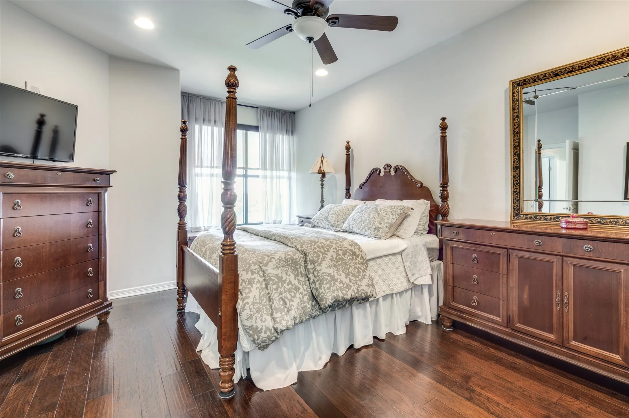 Primary bedroom with large window highlights wood floors
