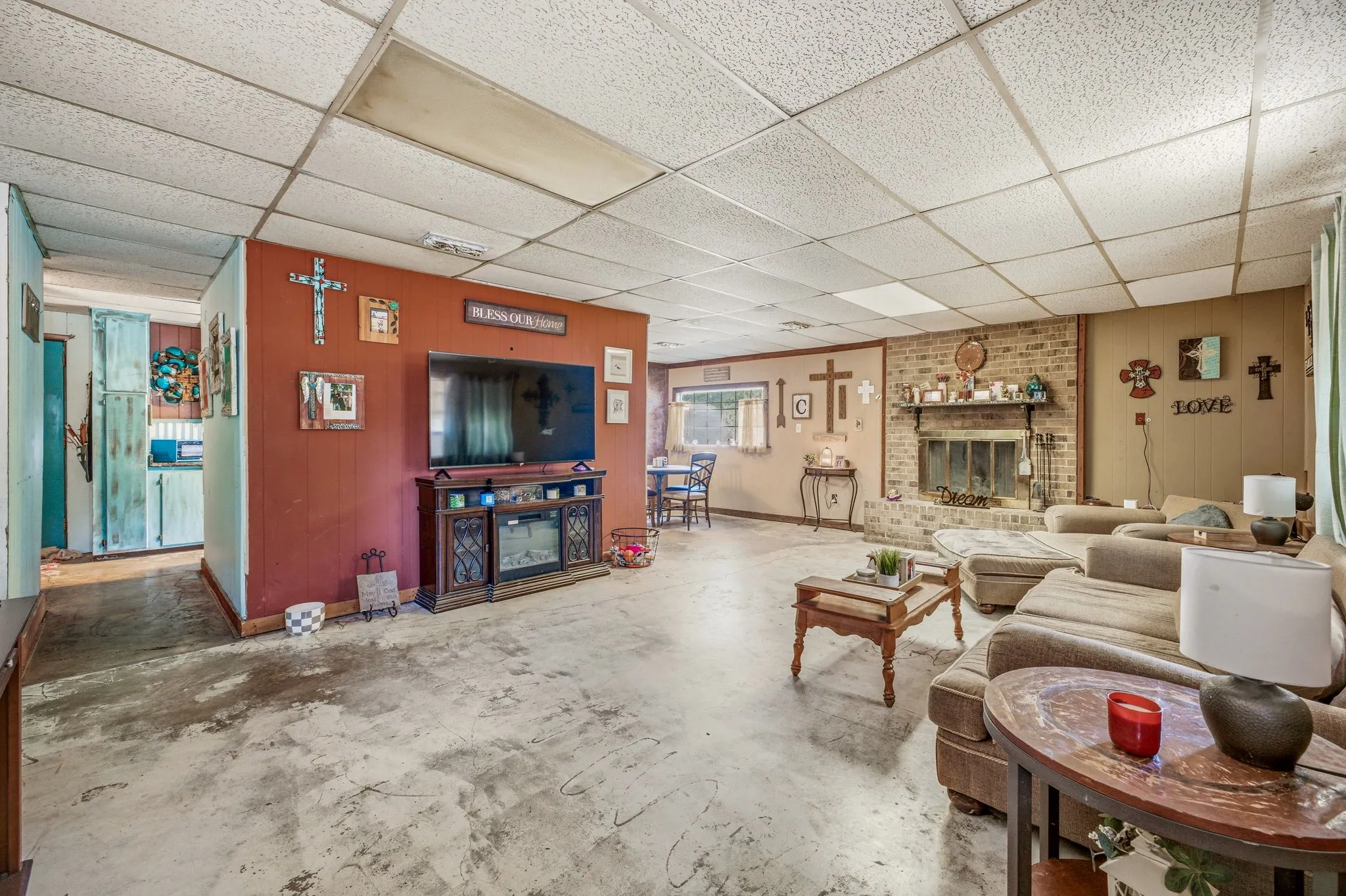 Spacious entertainment area featuring a brick-surround fireplace, drop ceiling, and concrete-finish flooring