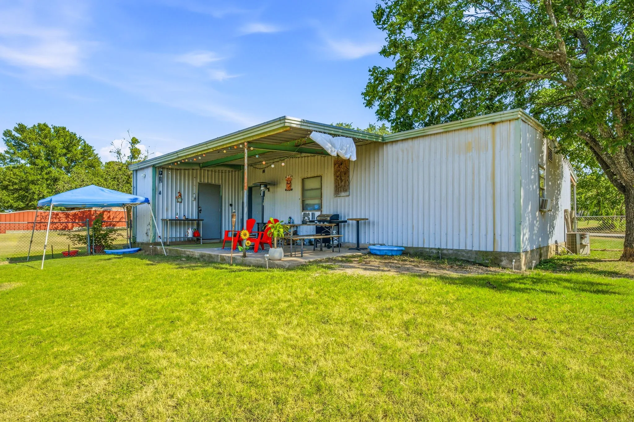 Expansive green space featuring a concrete patio, covered porch area, and mature trees providing natural shade