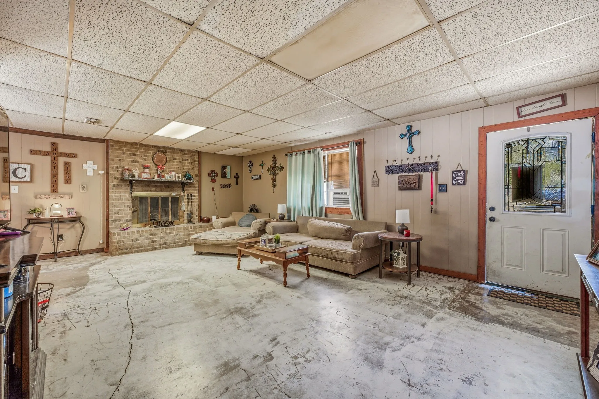 Living area featuring a brick fireplace, drop ceiling, and wood paneling