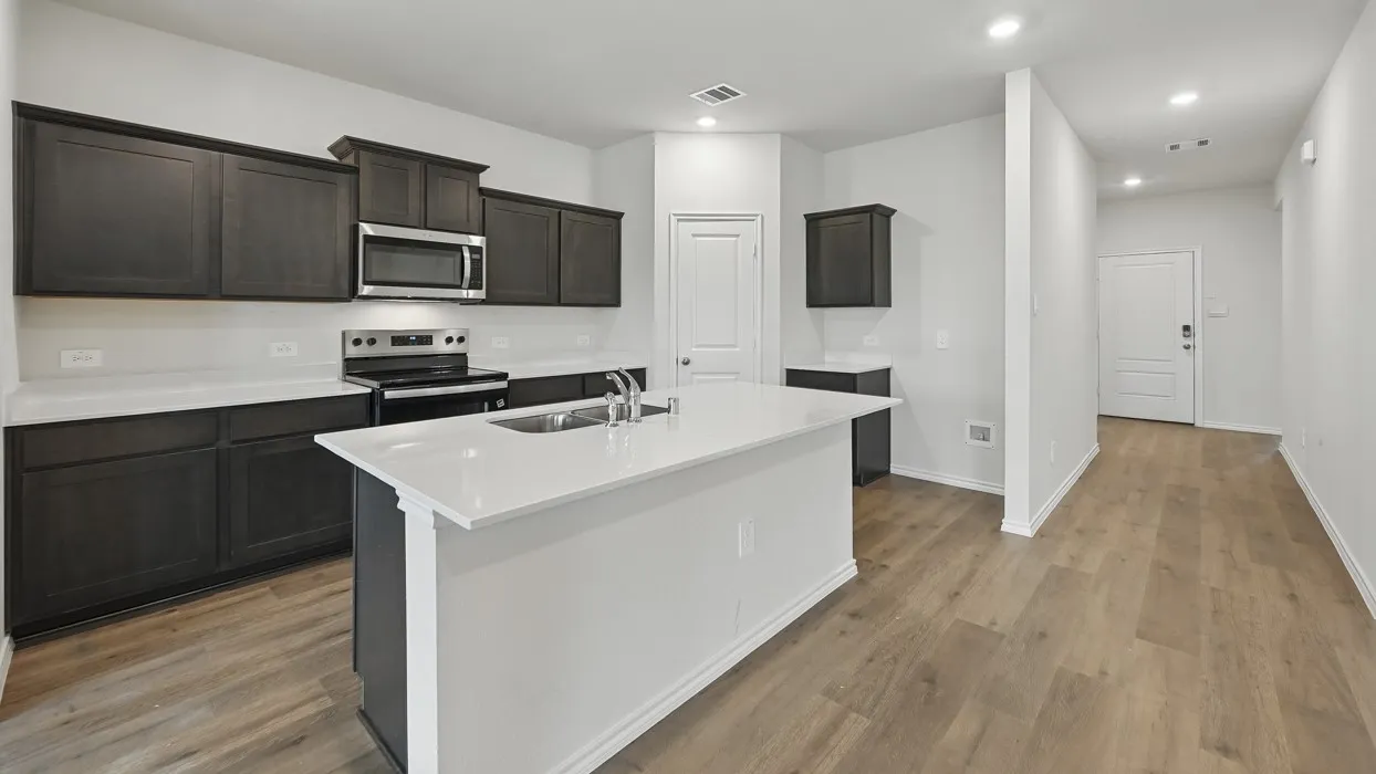 Kitchen featuring dark wood cabinetry, stainless steel appliances, white countertops, and a central island with an integrated sink