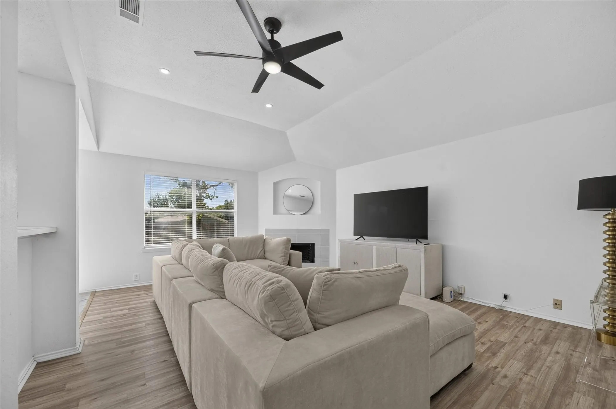 Vaulted ceiling with a contemporary ceiling fan, recessed lighting, wood-finish flooring, and a corner fireplace