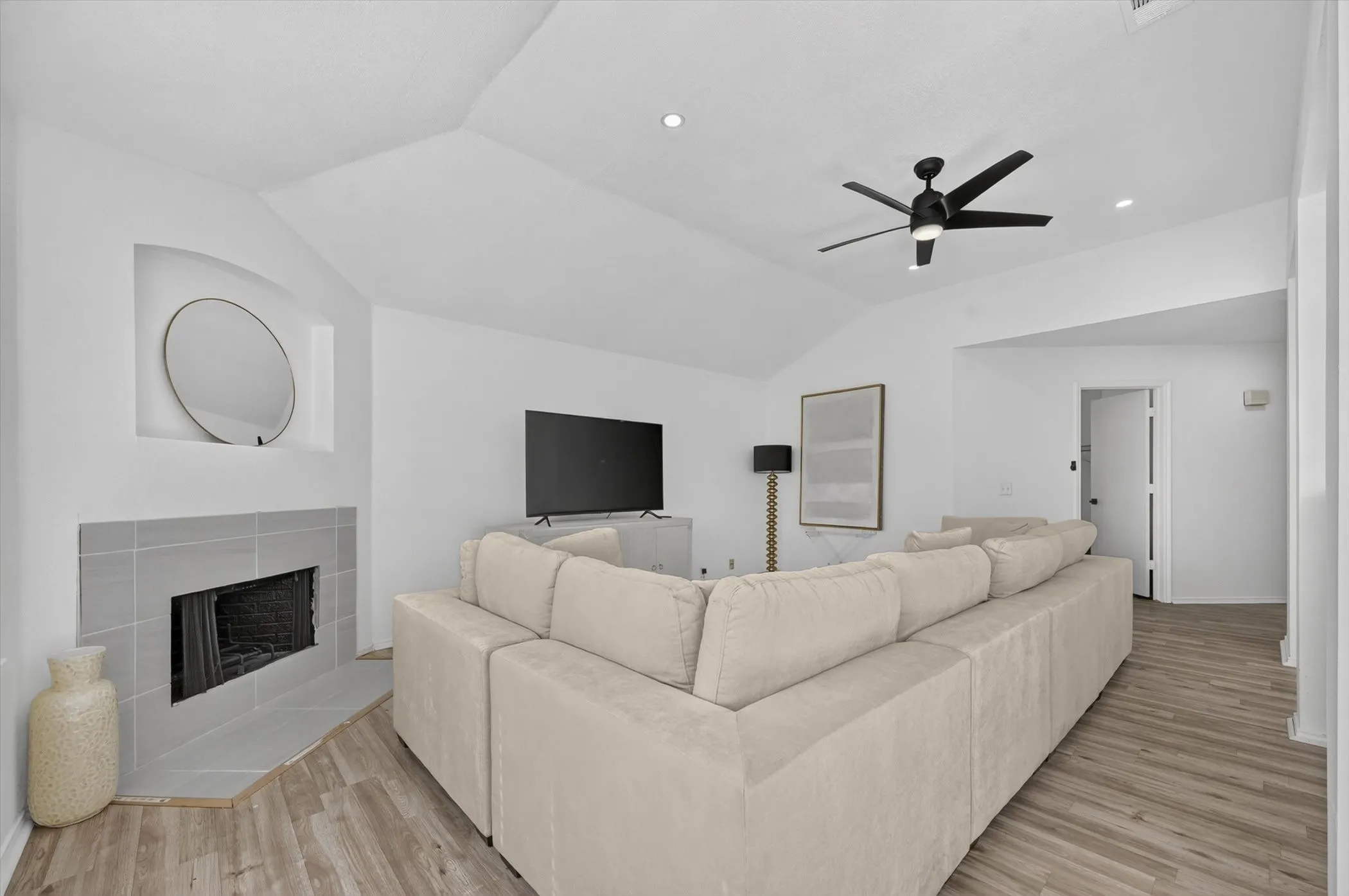 Vaulted ceiling living space featuring a tiled fireplace with an inset niche, wood-finish flooring, a ceiling fan with light, and recessed lighting