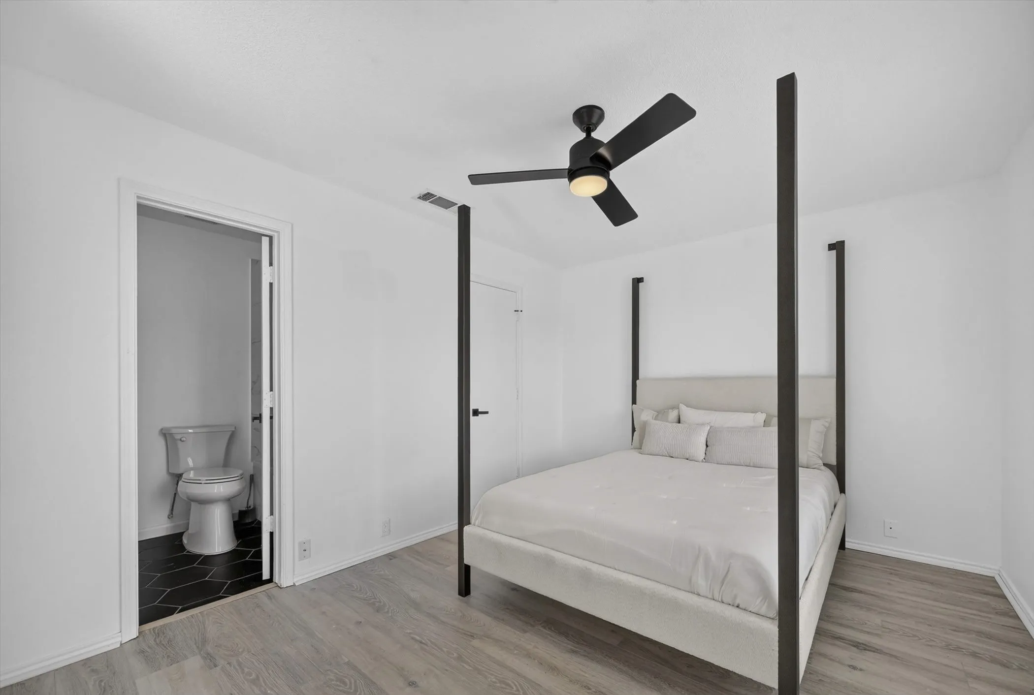 Bright room with light wood-finish flooring, white walls, and a black ceiling fan