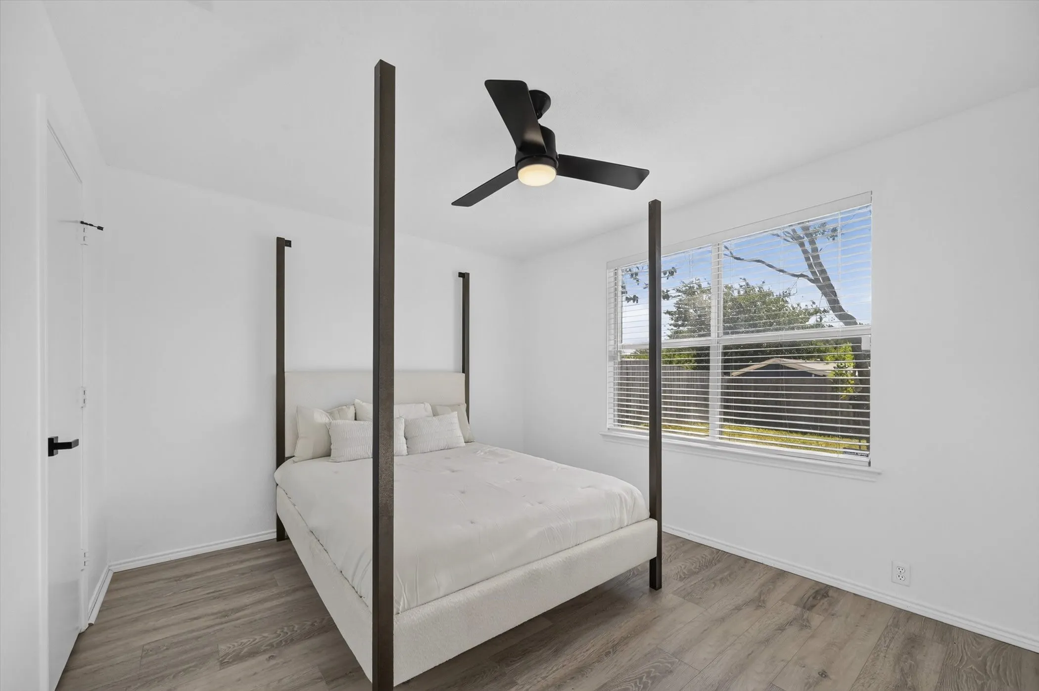 Bright room featuring wood-finish flooring, a contemporary ceiling fan with integrated lighting, and a large window with horizontal blinds