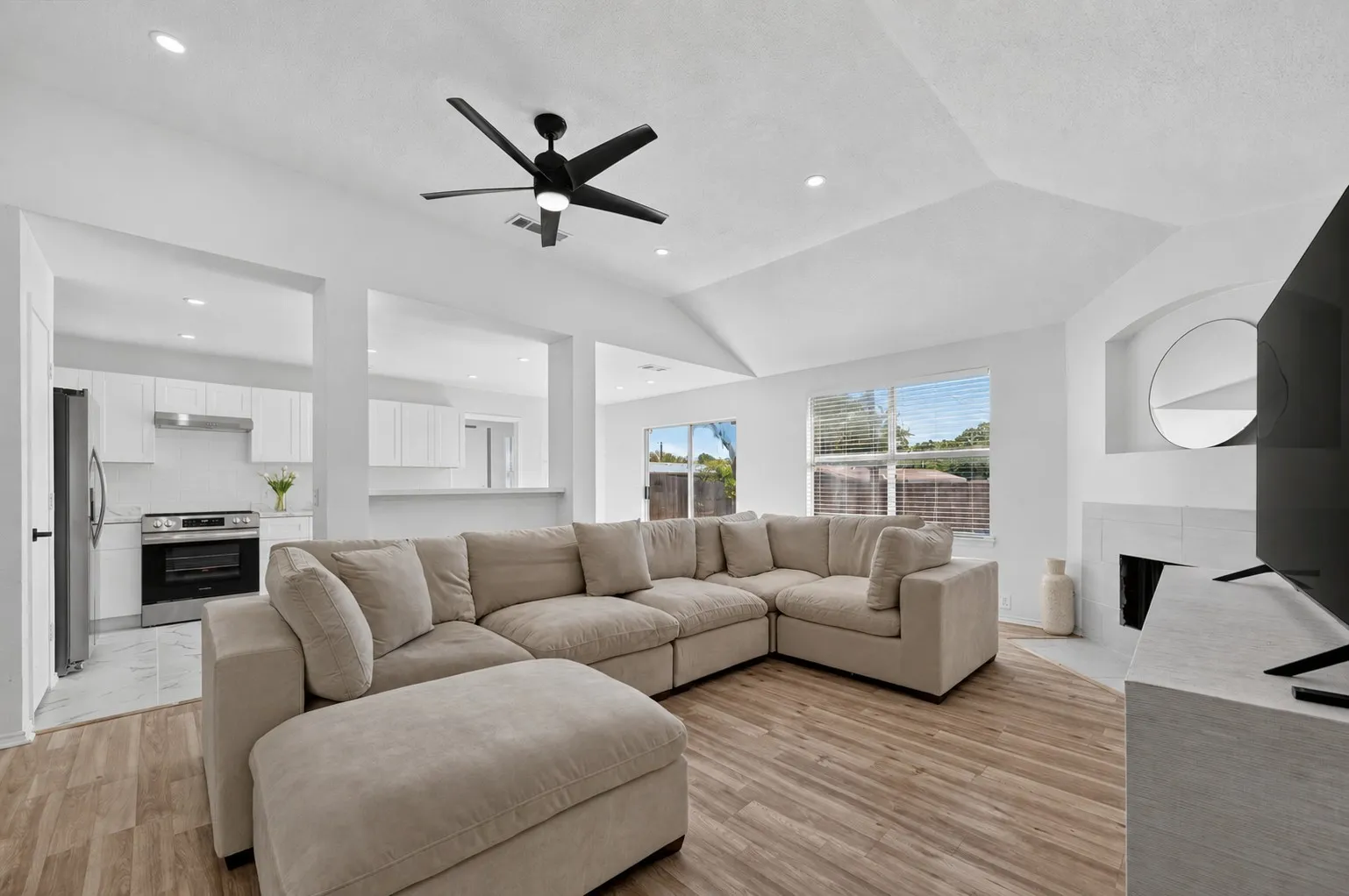 Spacious living area featuring vaulted ceilings, wood-finish flooring, recessed lighting, and a modern ceiling fan