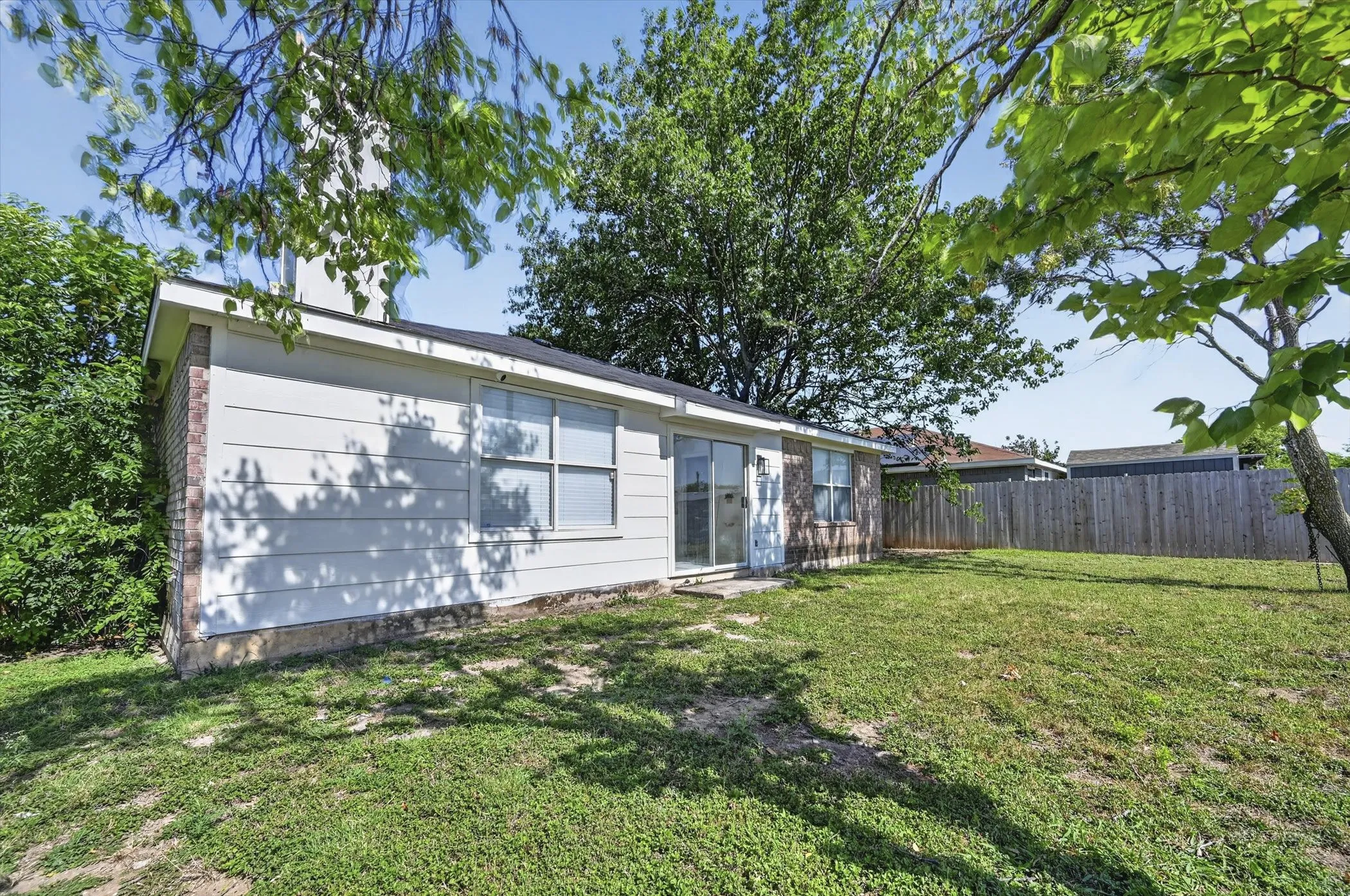 Expansive backyard featuring a manicured lawn, established trees, and a privacy fence