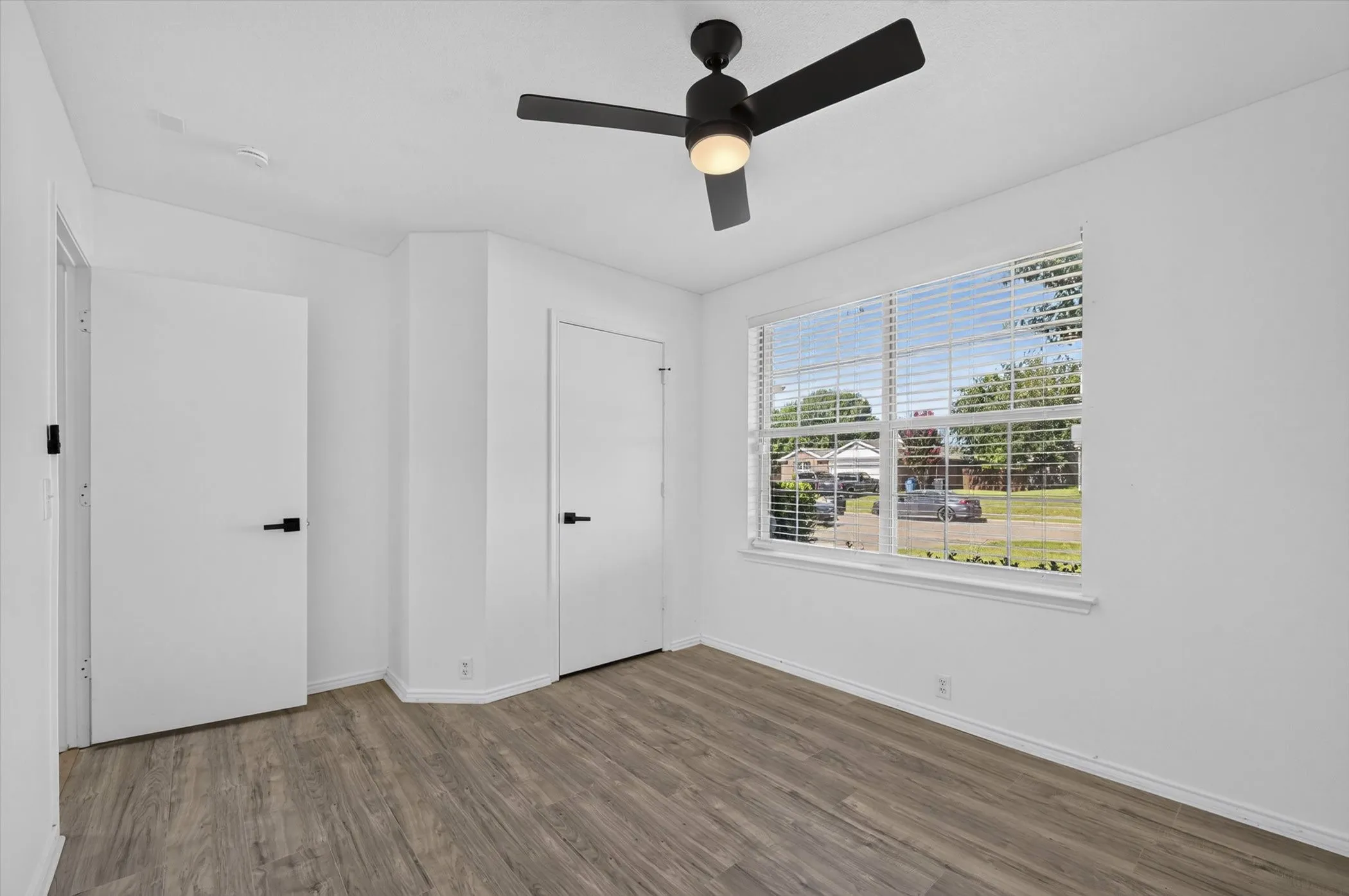 White walls complement wood-finish flooring in this space, featuring a modern ceiling fan with integrated lighting