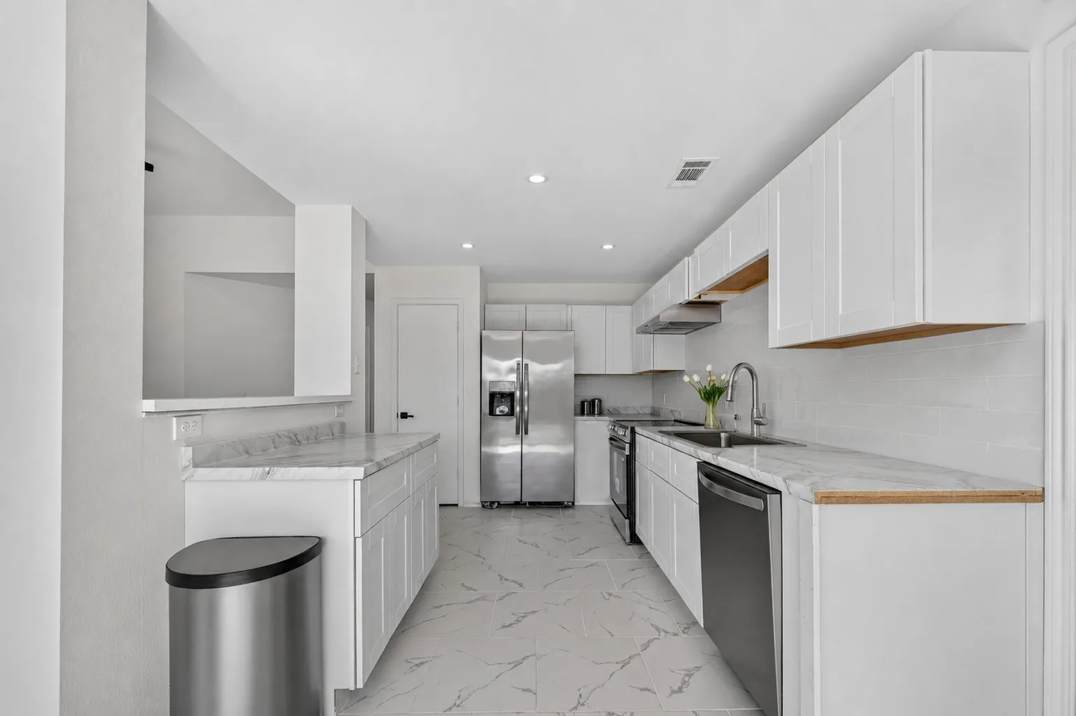 Bright kitchen featuring white shaker cabinetry, stainless steel appliances, a subway tile backsplash, light-toned countertops, and recessed lighting
