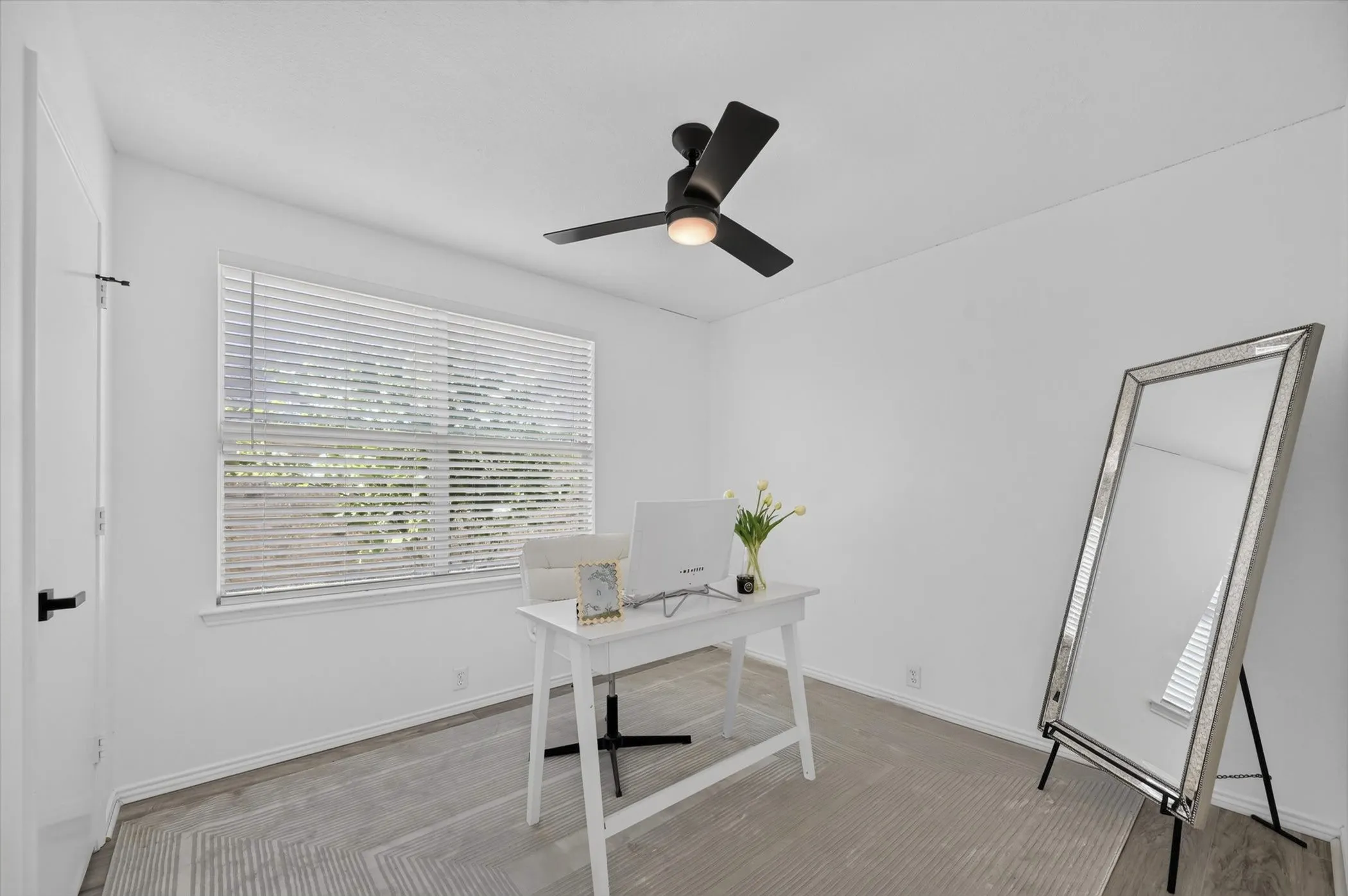 Bright room featuring white walls, a black ceiling fan with integrated lighting, and a large window with white blinds