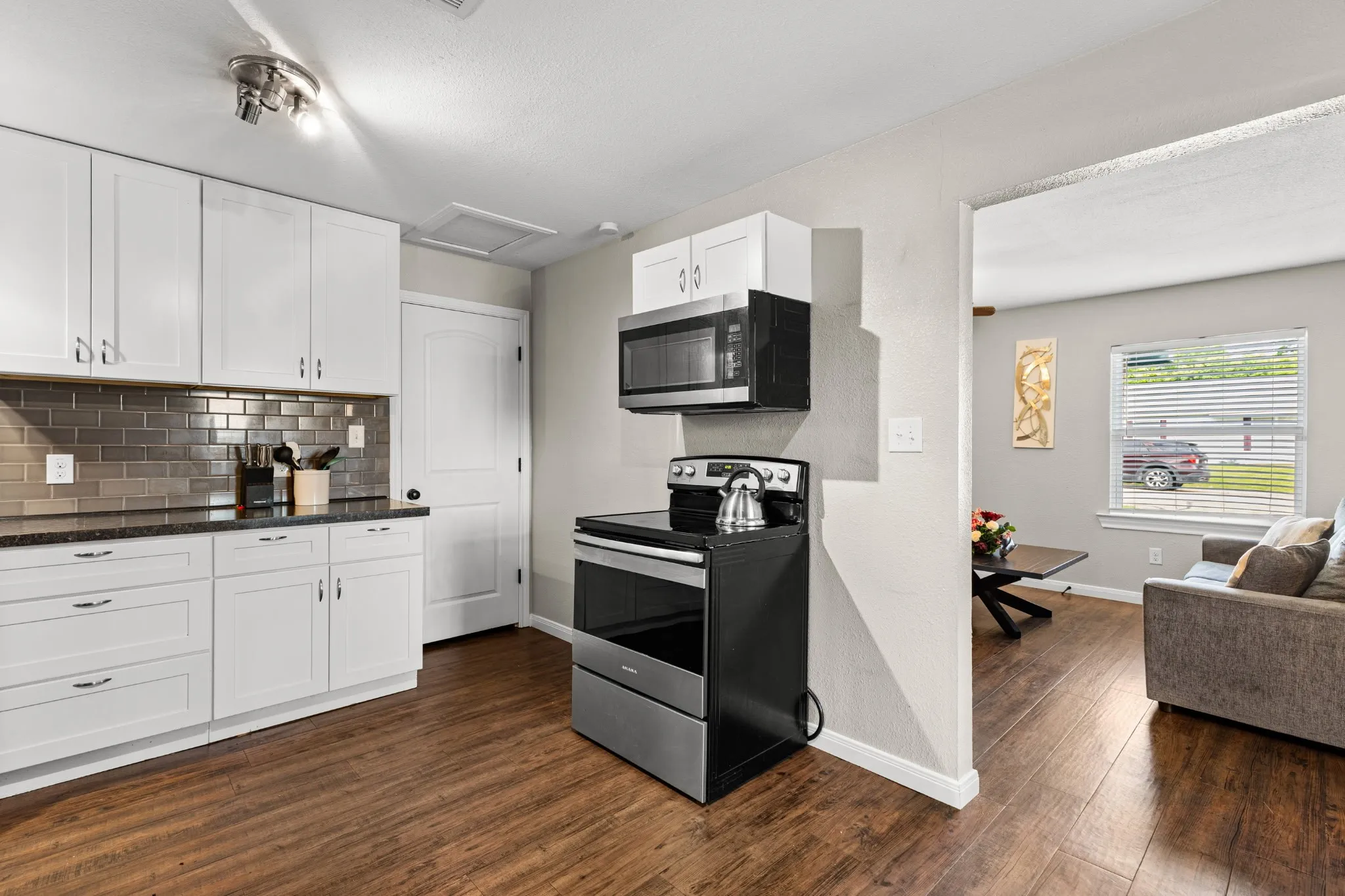 Kitchen featuring white cabinetry, dark countertops, a metallic subway tile backsplash, stainless steel appliances, and wood-finish flooring