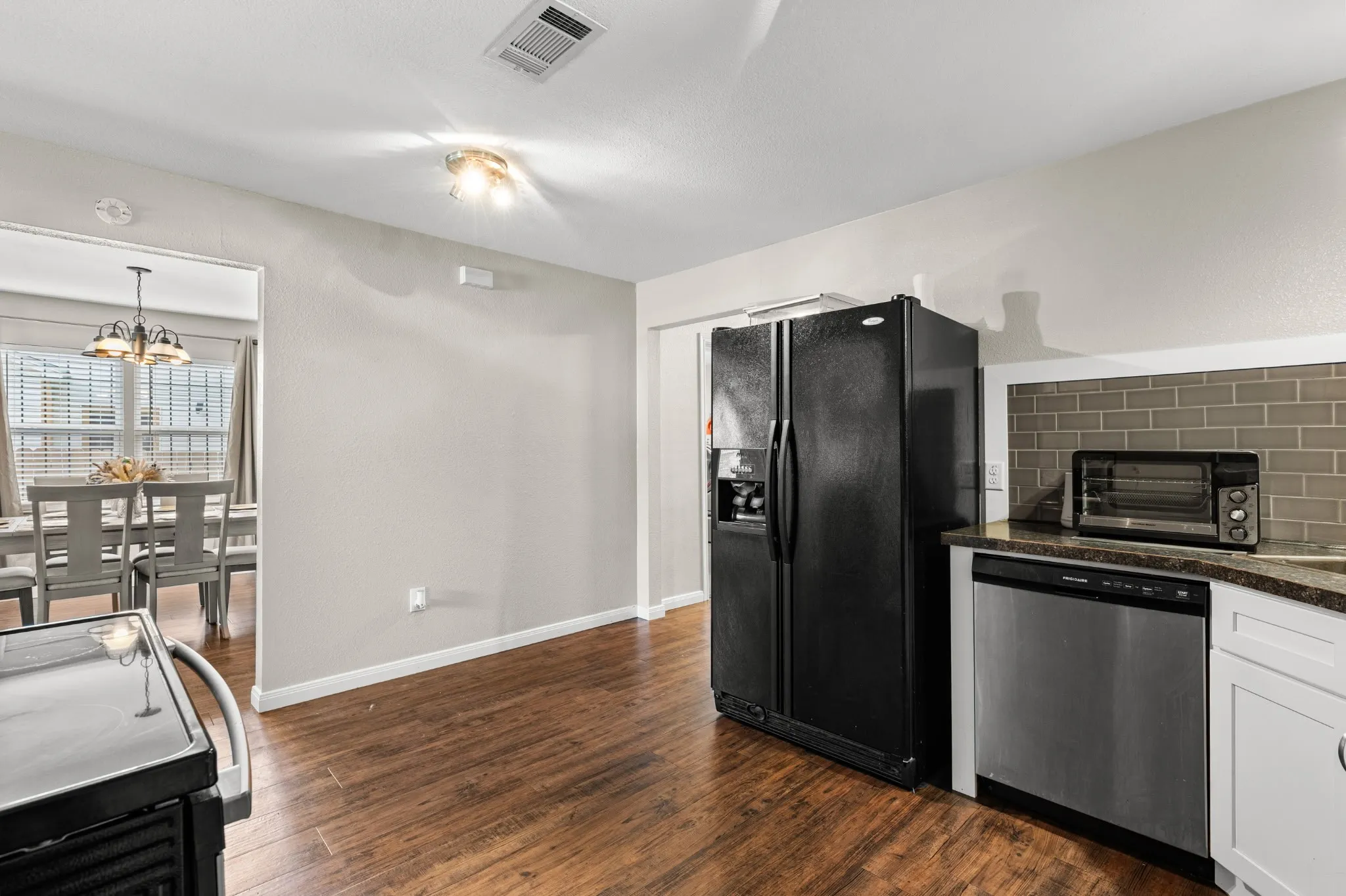 Kitchen featuring wood-finish flooring, white cabinetry, a dark subway tile backsplash, and a stainless-steel dishwasher