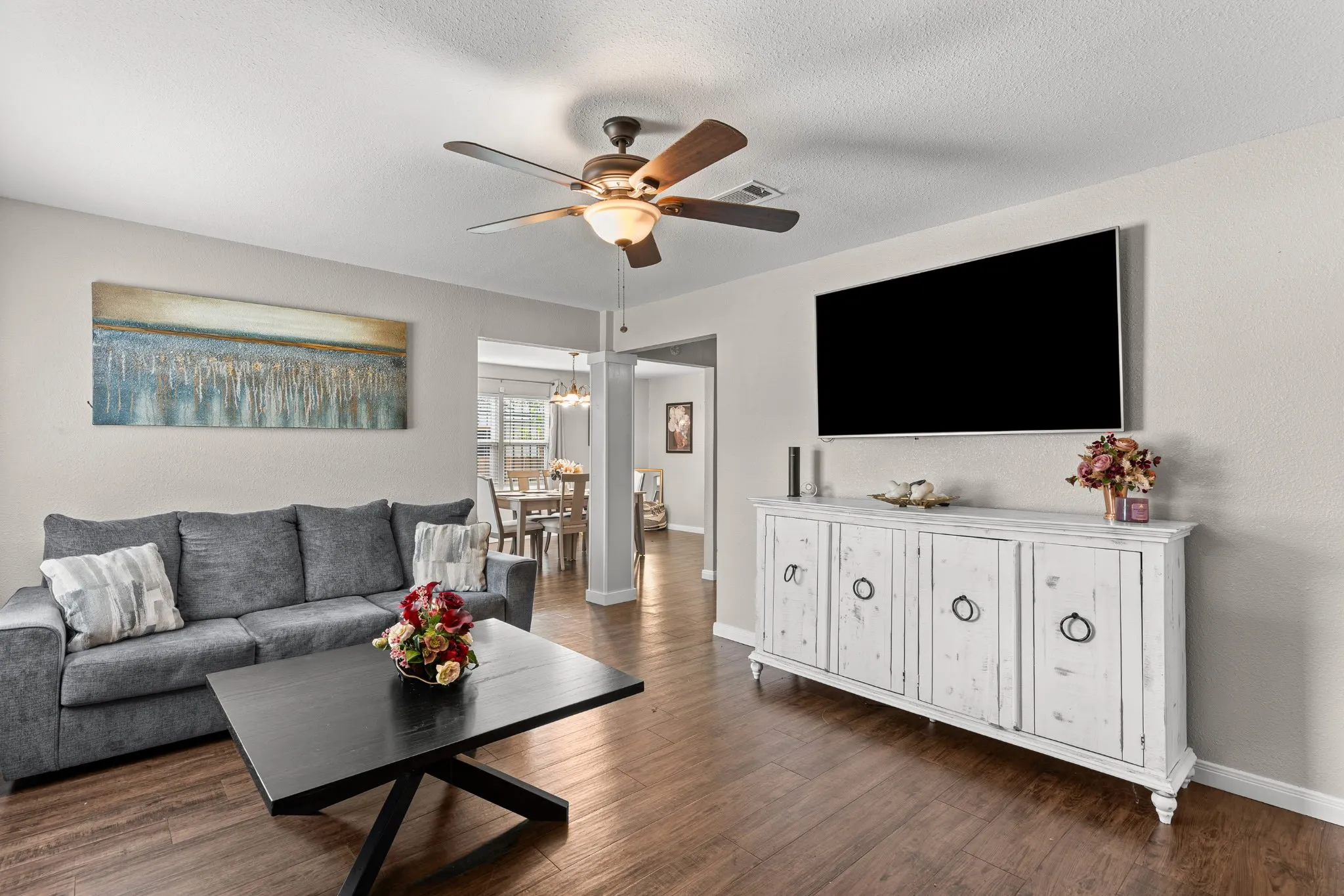 Open-concept living space featuring wood-finish flooring, a ceiling fan with integrated lighting, and neutral wall tones