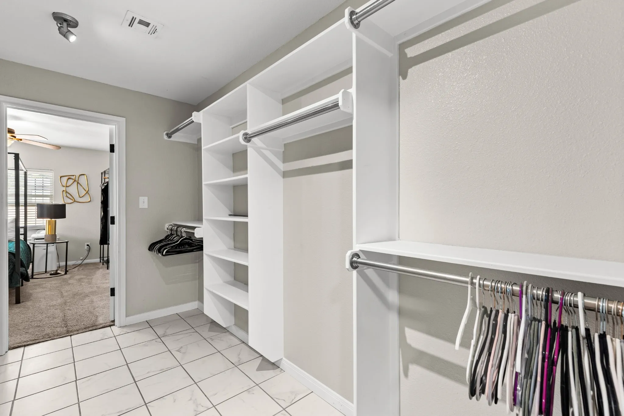 Walk-in closet featuring white built-in shelving, multiple hanging rods, and tile flooring