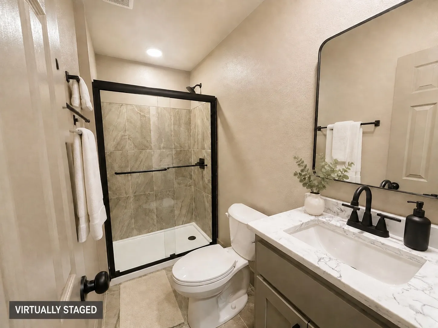 Enclosed shower with tiled surround, single vanity with countertop, and black fixtures