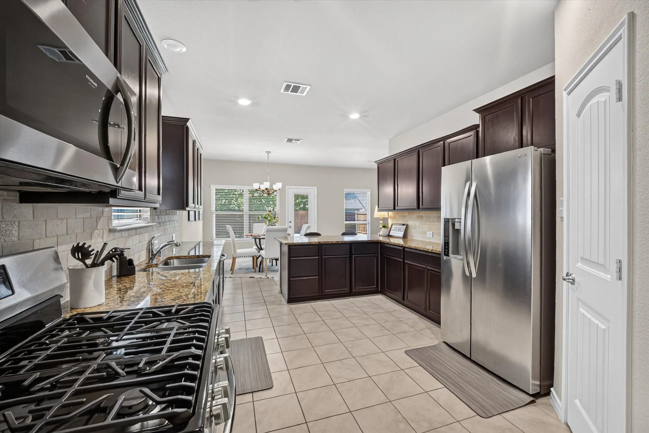 Kitchen featuring dark wood cabinetry, stainless steel appliances, granite countertops, and light-colored tile flooring