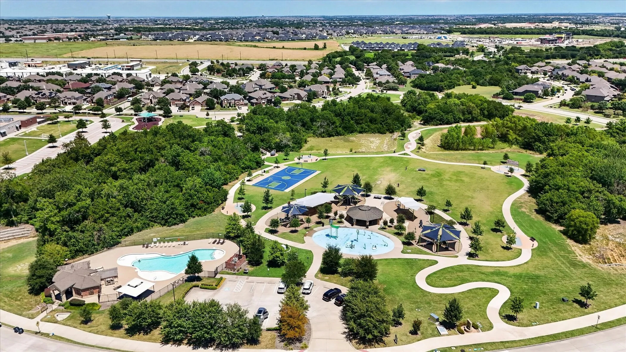 Community green space featuring a large swimming pool, tennis courts, splash pad, and winding paved pathways