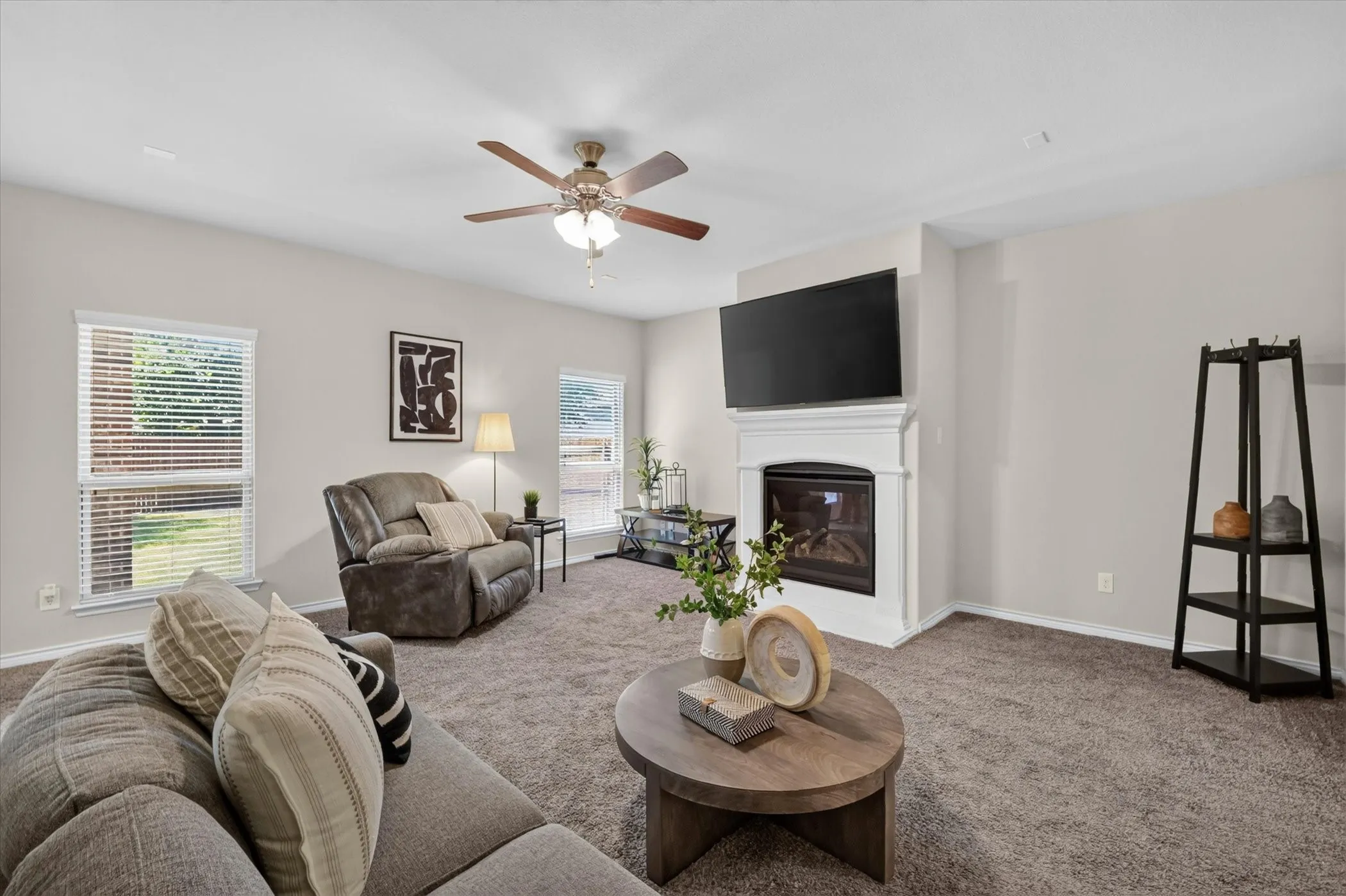 Living area featuring a floor-to-ceiling fireplace with a white mantel, neutral wall paint, and a ceiling fan with light fixture