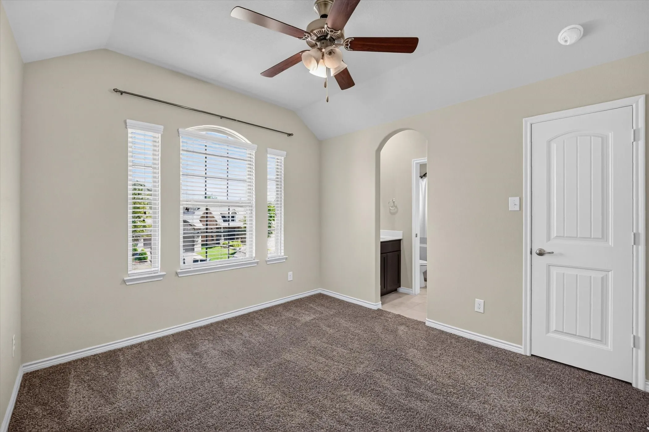 Vaulted ceiling with a ceiling fan, arched doorway, and windows with blinds