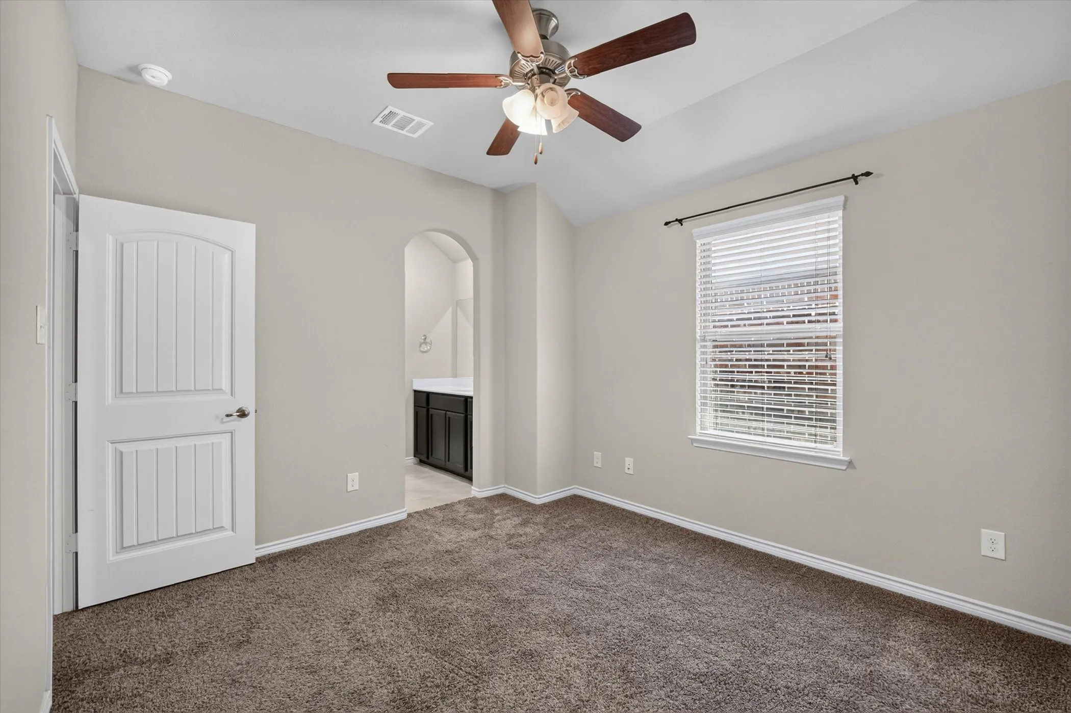 Neutral-toned bedroom featuring vaulted ceilings, a ceiling fan with light fixture, and plush carpet flooring