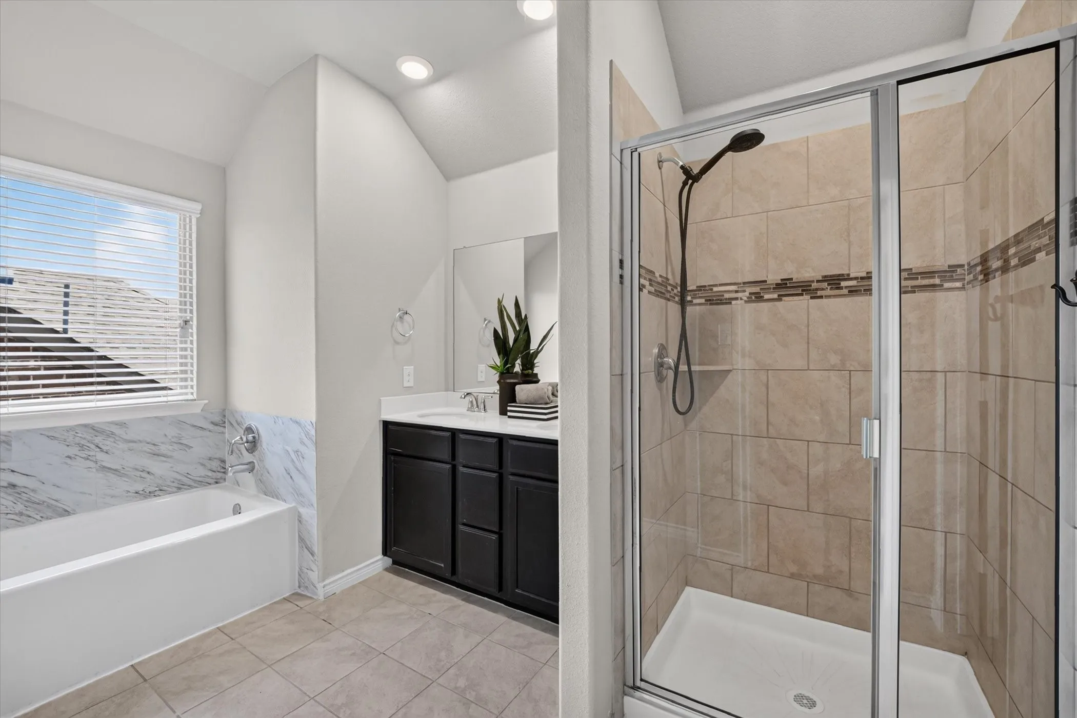 Bathroom featuring a glass-enclosed shower with tiled walls and decorative accent band, a white soaking tub with a tiled surround, a dark wood-finish vanity with a white countertop and integrated sink, and recessed lighting