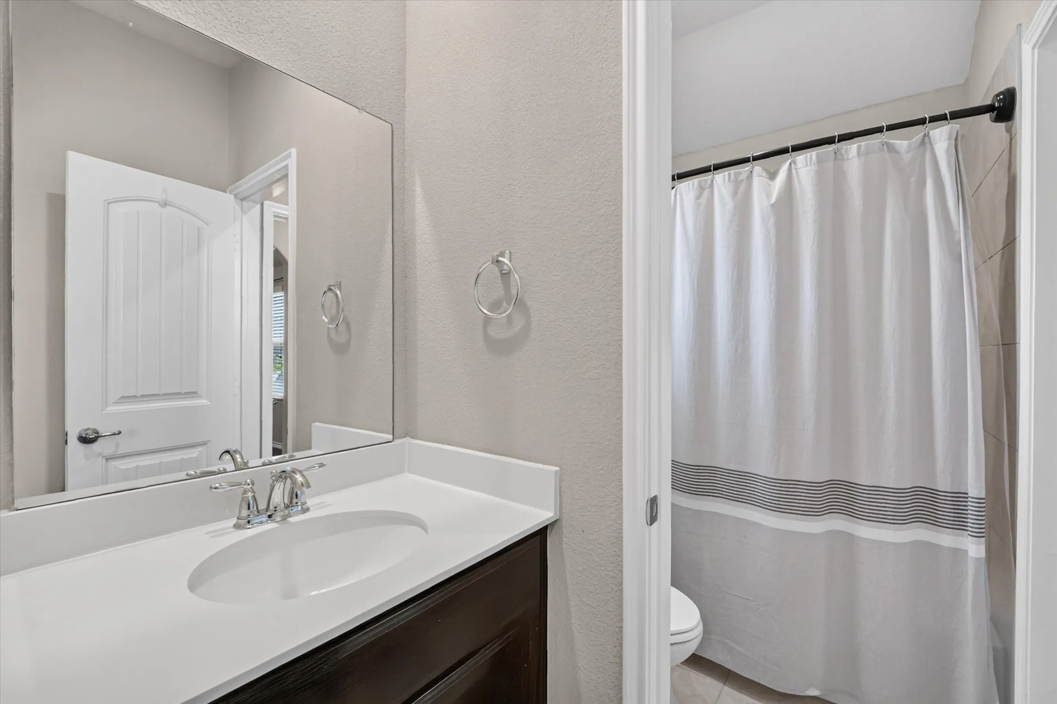 Bathroom featuring a dark wood-finish vanity with an integrated white sink, chrome faucet, and a large wall-mounted mirror