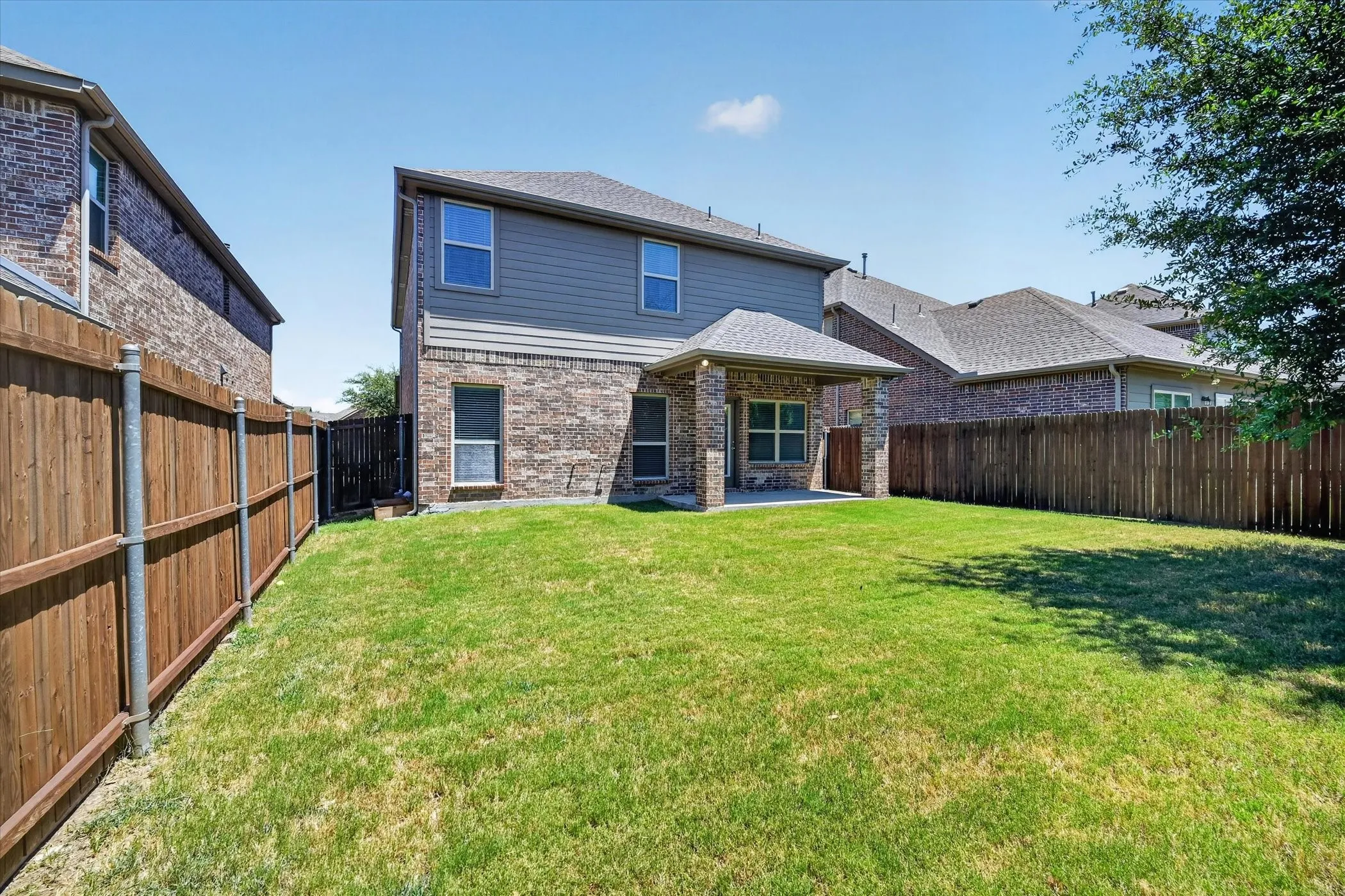 Expansive backyard featuring a manicured lawn, full privacy fencing, and a covered patio with brick and stone columns