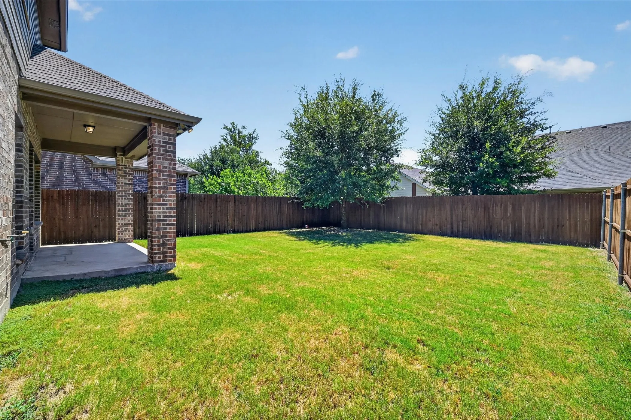 Spacious backyard featuring a substantial lawn, perimeter privacy fencing, and two mature trees