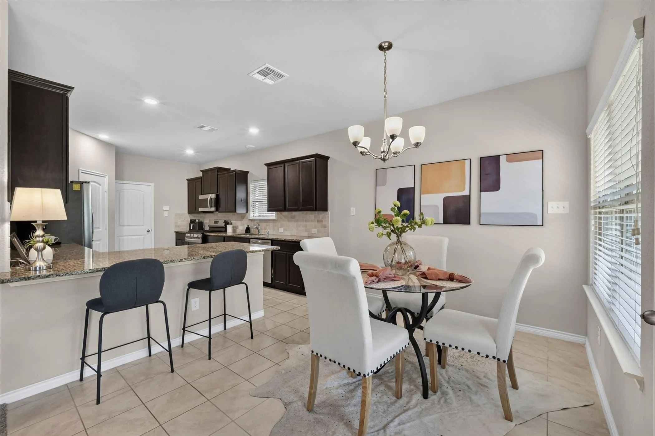 Open-concept kitchen and dining area featuring tile flooring, a breakfast bar with stone countertop, dark wood-finish cabinetry, and stainless steel appliances