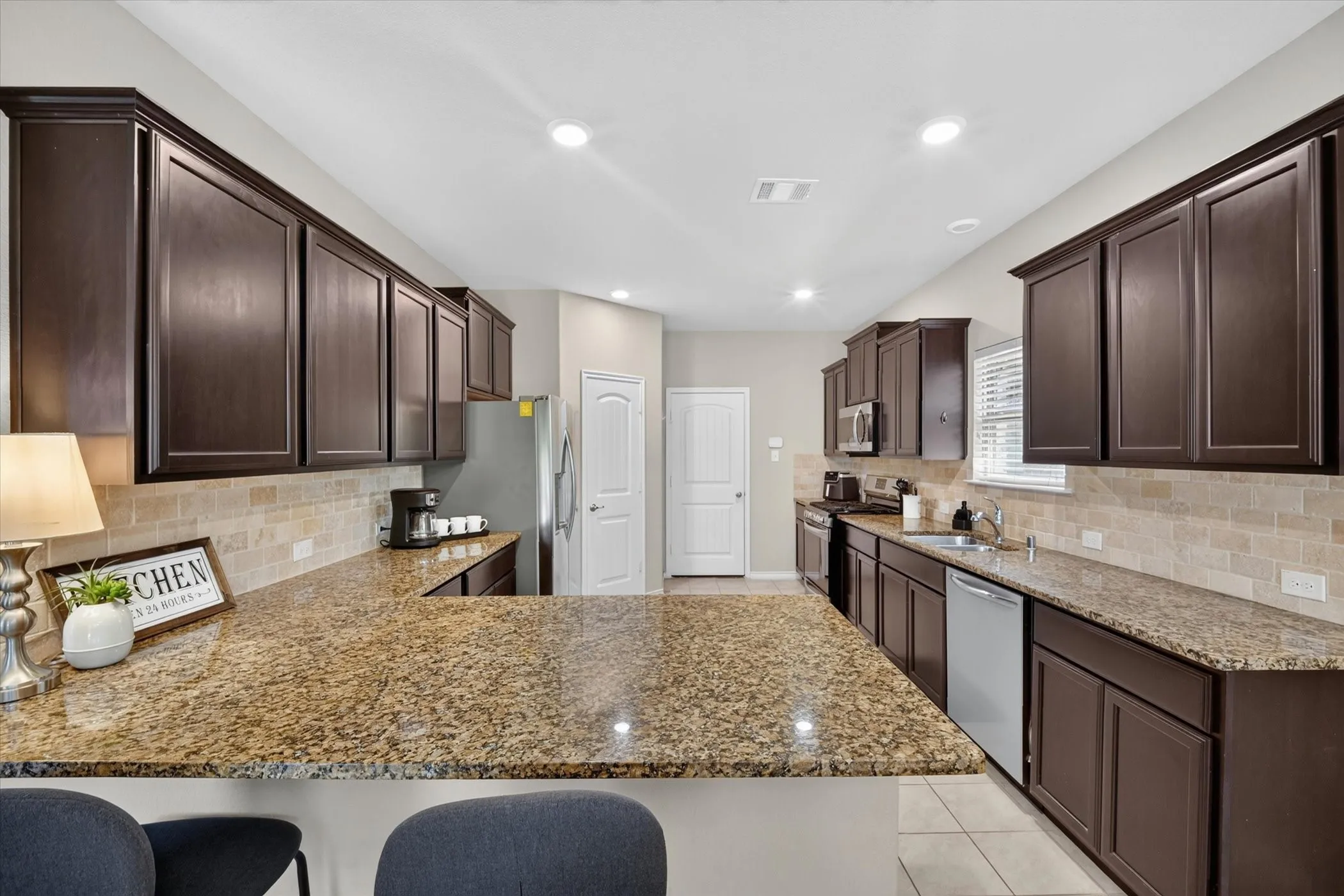 Kitchen featuring an expansive island with granite countertops, dark wood cabinetry, a tile backsplash, and recessed lighting