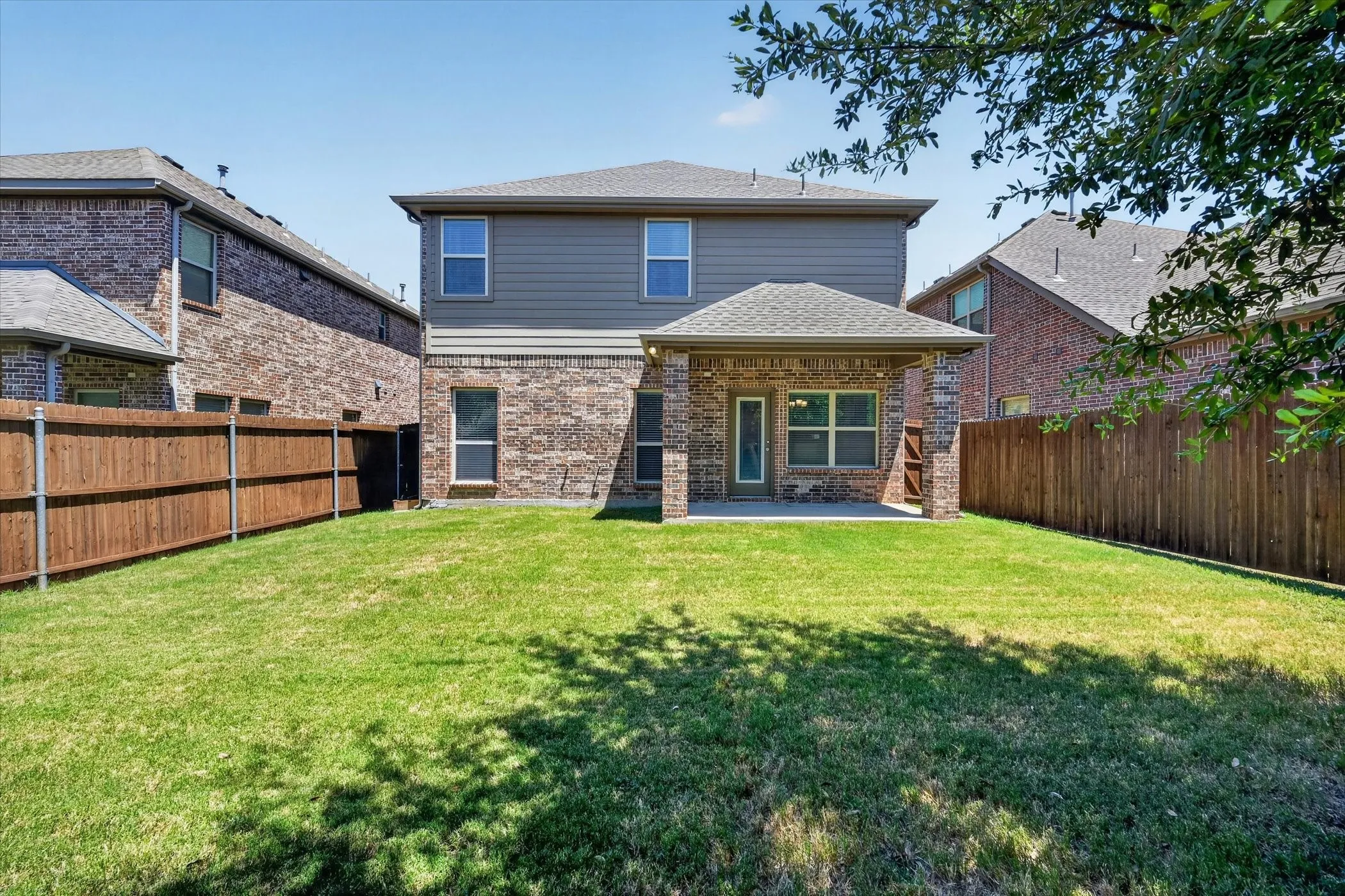 Expansive backyard featuring a covered patio, a full privacy fence, and a two-story exterior with brick and siding finishes