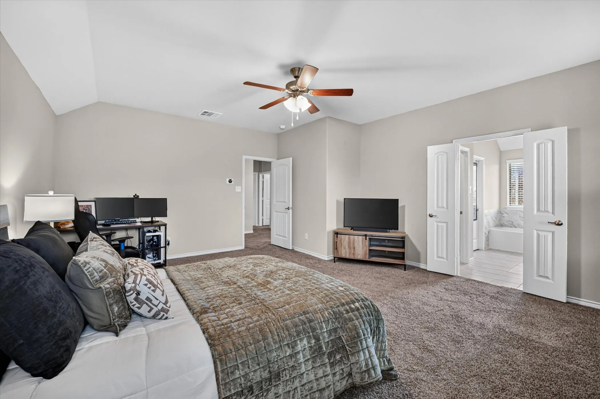 Spacious bedroom featuring vaulted ceilings, neutral-toned walls, and plush carpeting