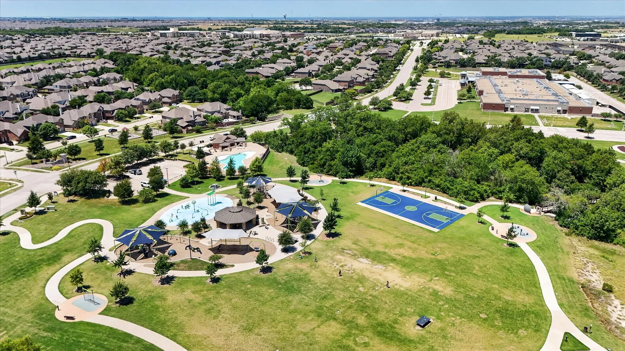Expansive community park featuring a splash pad, swimming pool, shaded playground areas, and a basketball court