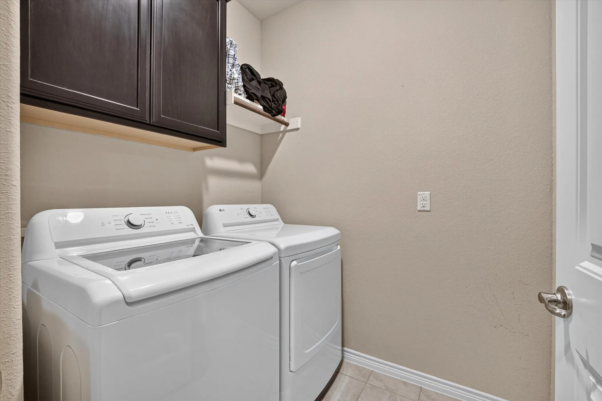 Laundry area featuring dark wood-finish cabinetry, an open wall shelf, and light neutral-toned walls