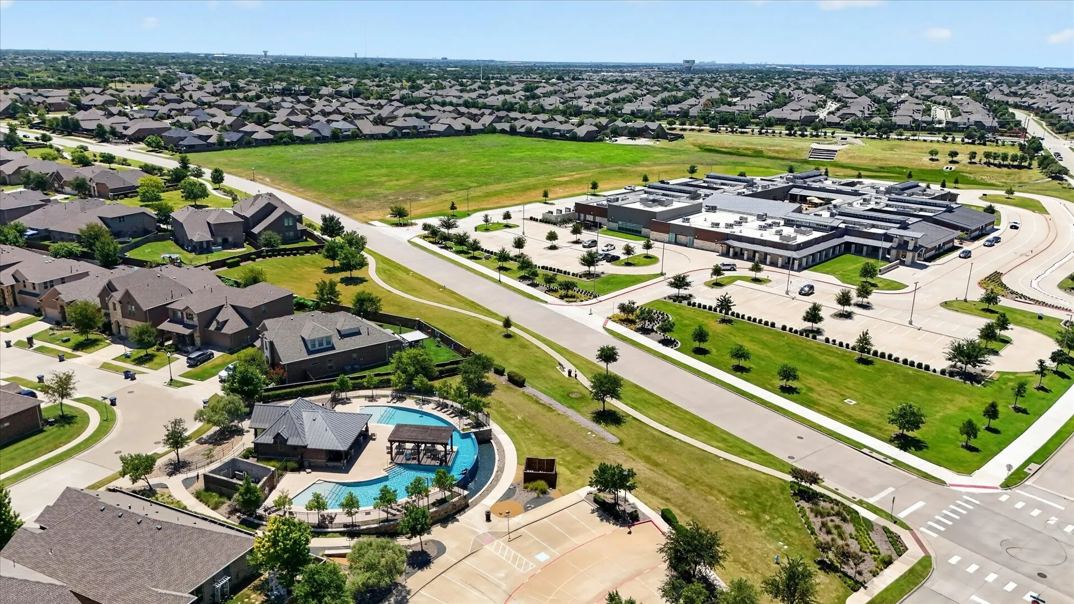 Expansive neighborhood featuring a community pool with an adjacent pavilion, modern residential architecture, and a nearby institutional building with ample parking