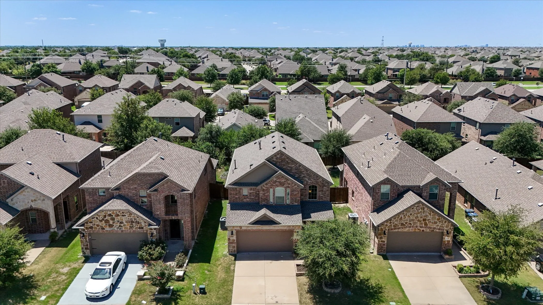 Aerial perspective showcasing a residential neighborhood with uniformly designed homes featuring brick and stone exteriors, asphalt shingle roofs, and attached garages